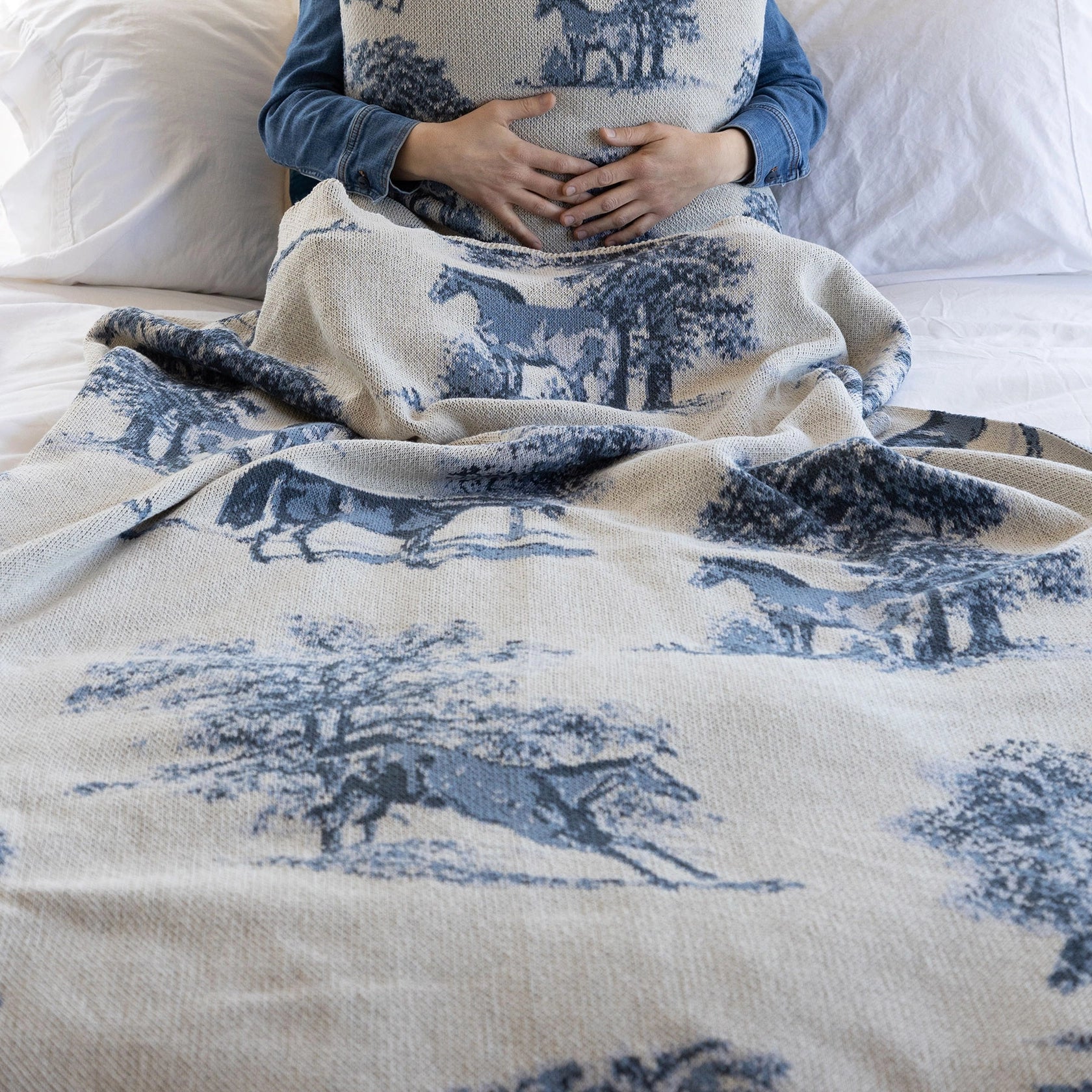 Equestrian Toile Throw Blanket in Blue used as a bed quilt and a man is underneath holding the matching pillow.