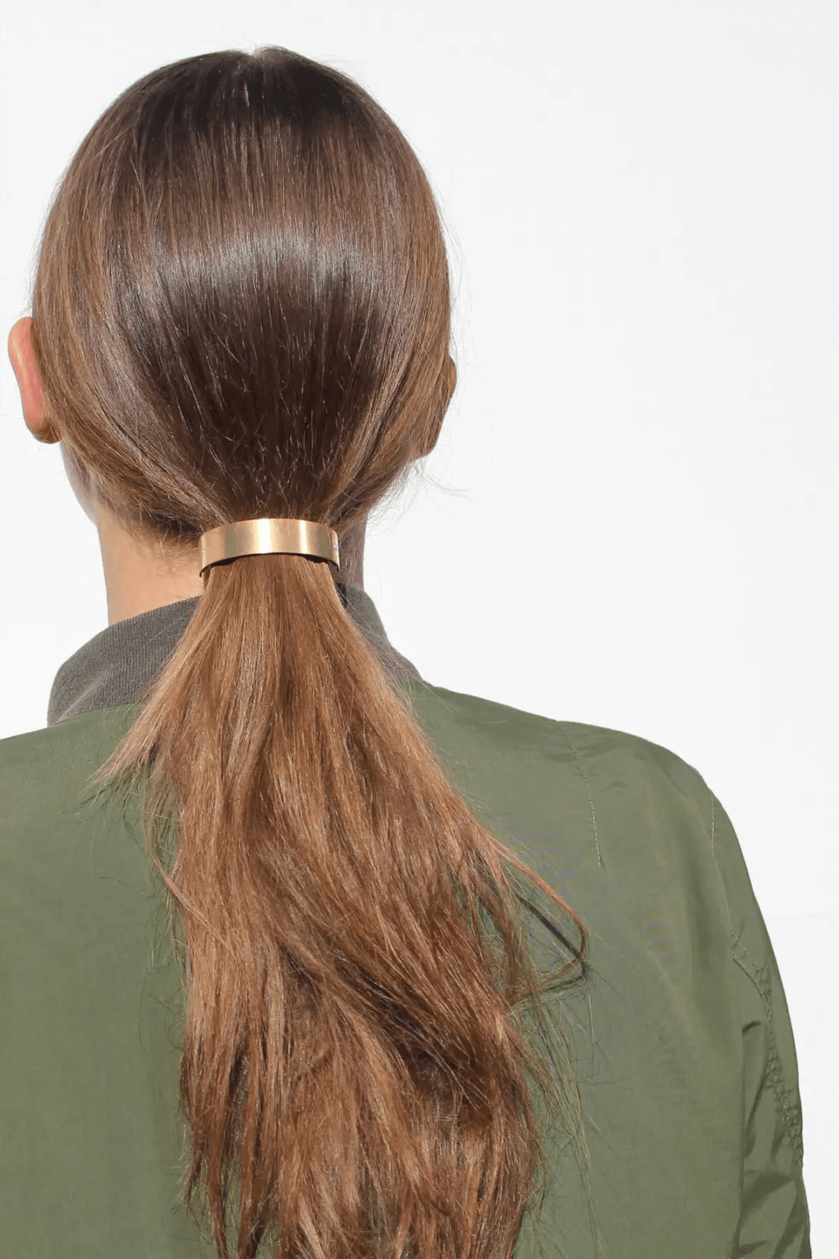 Person with a high ponytail wearing a gold hair tie on a white background