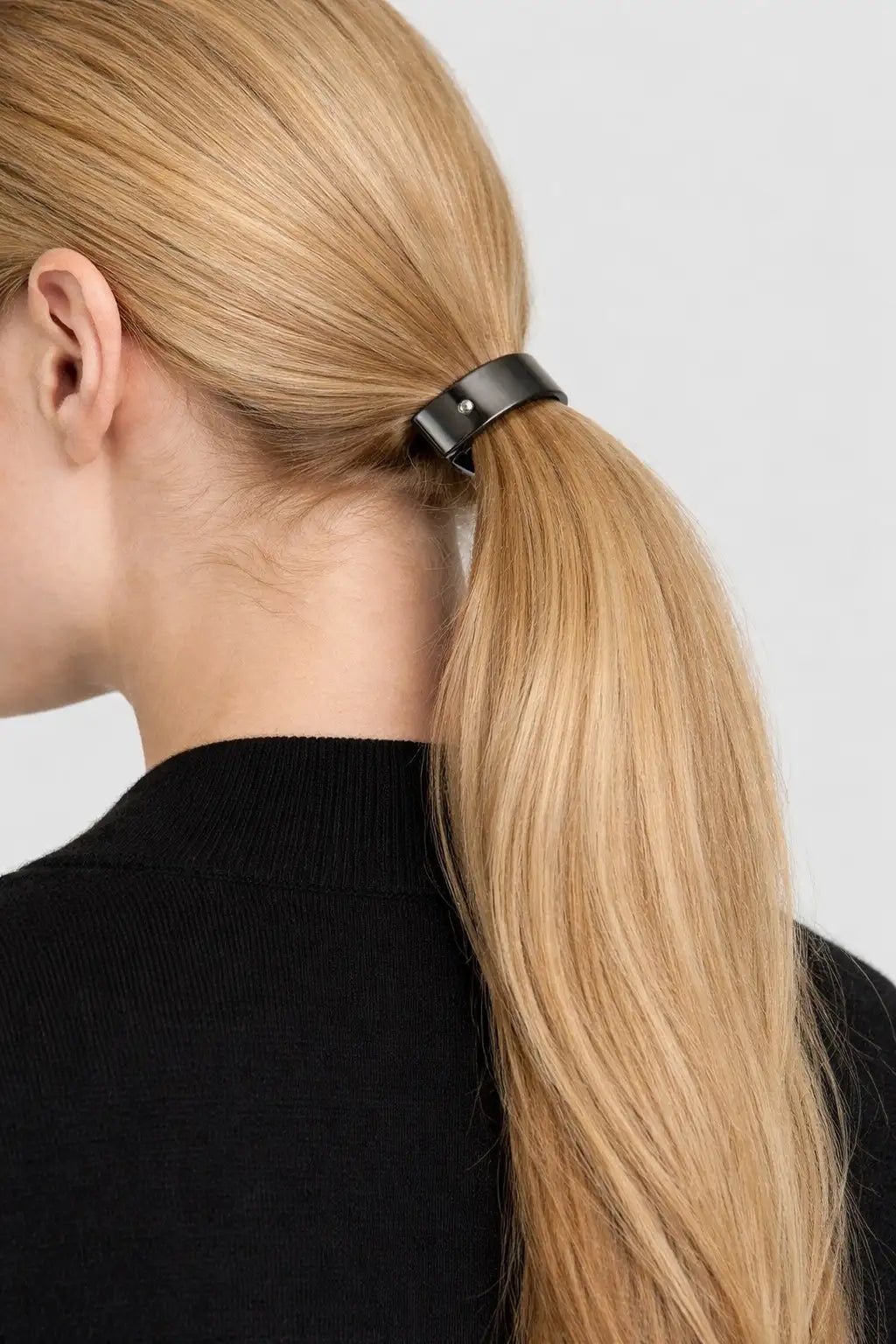 Woman with blonde hair in a ponytail wearing a silver black barrette against a white background
