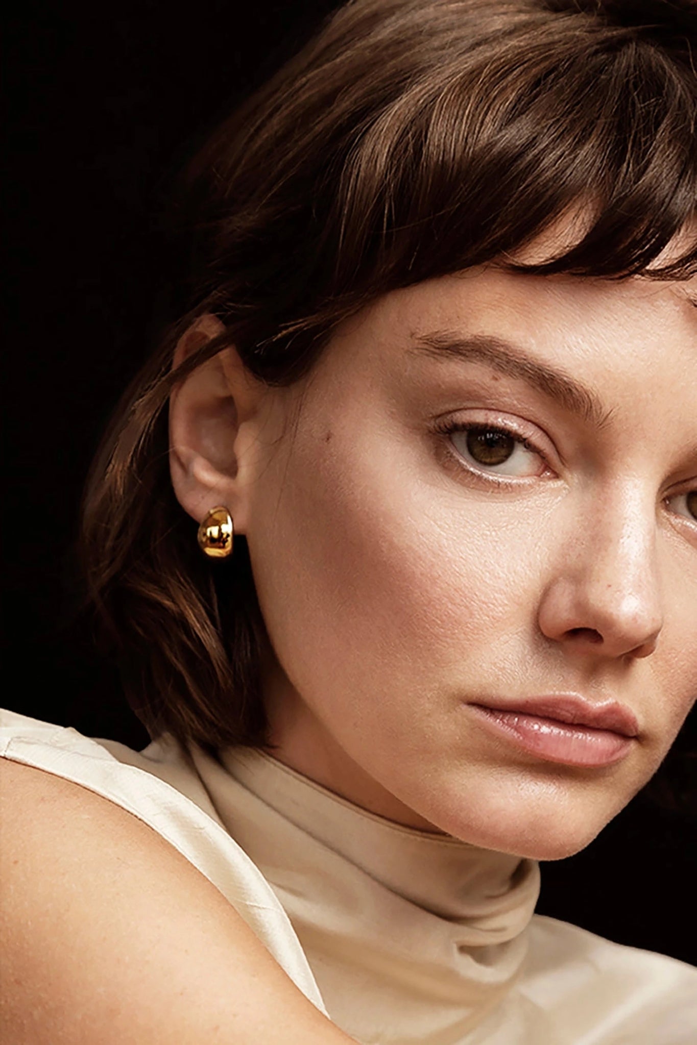 A model is wearing the Golden Serenity Huggie Hoop Earrings with her right ear showing in the photo.
