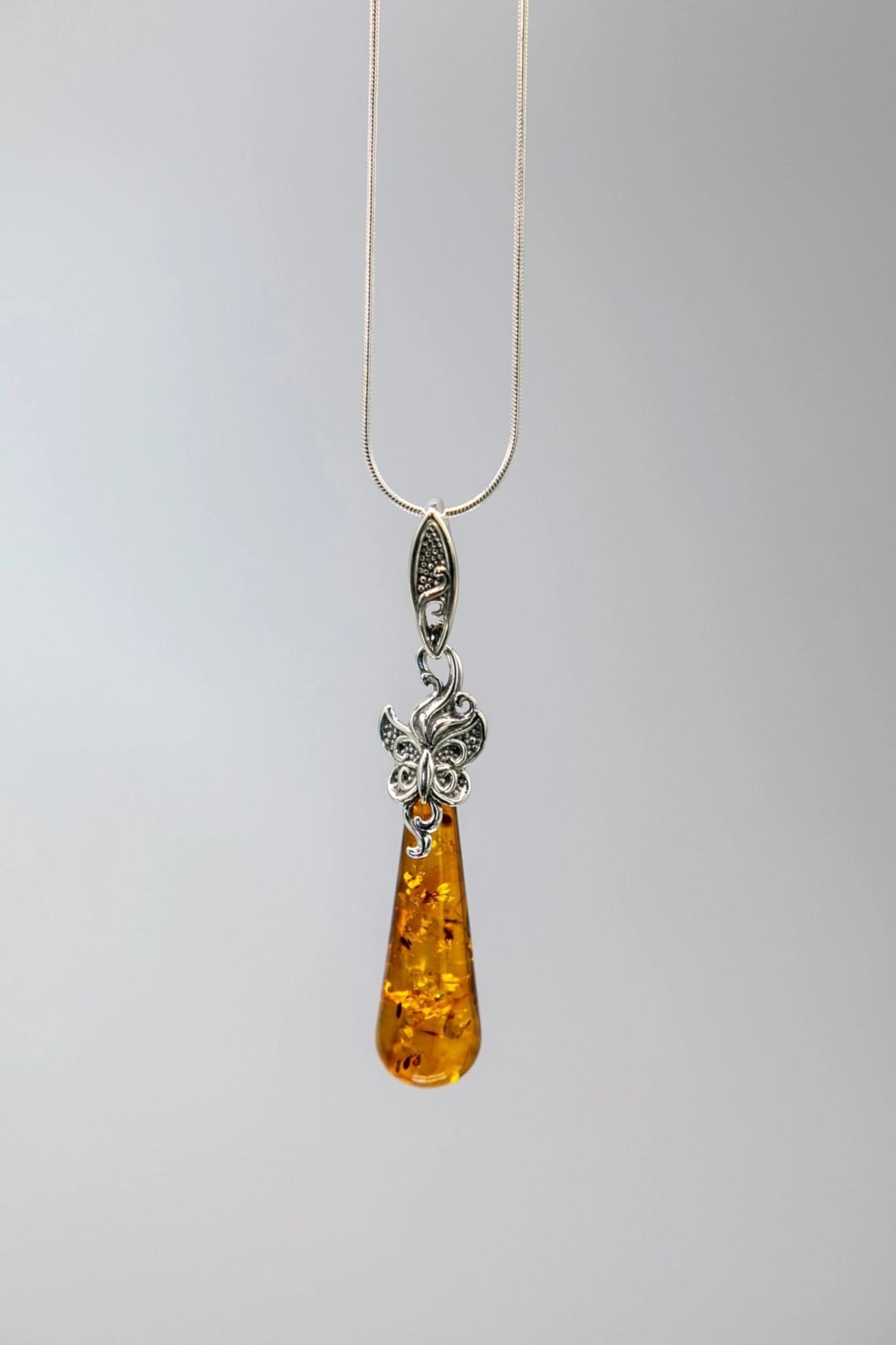 Necklace with an amber teardrop pendant and silver chain on a gray background