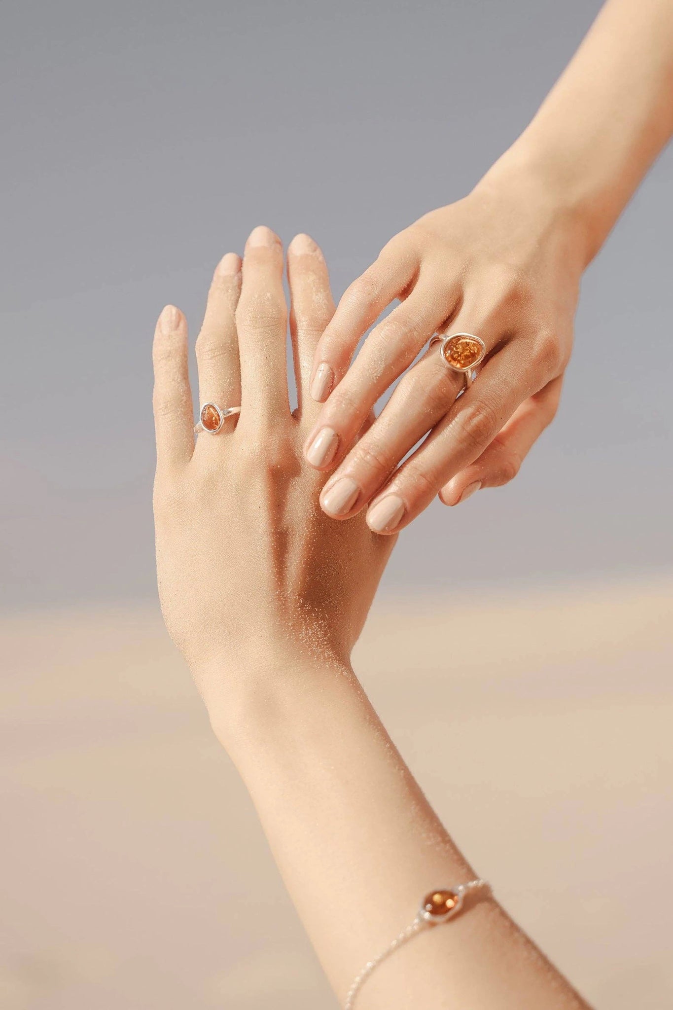 A female model's hands both wearing the Honey Baltic Amber Element Solitaire Adjustable Ring