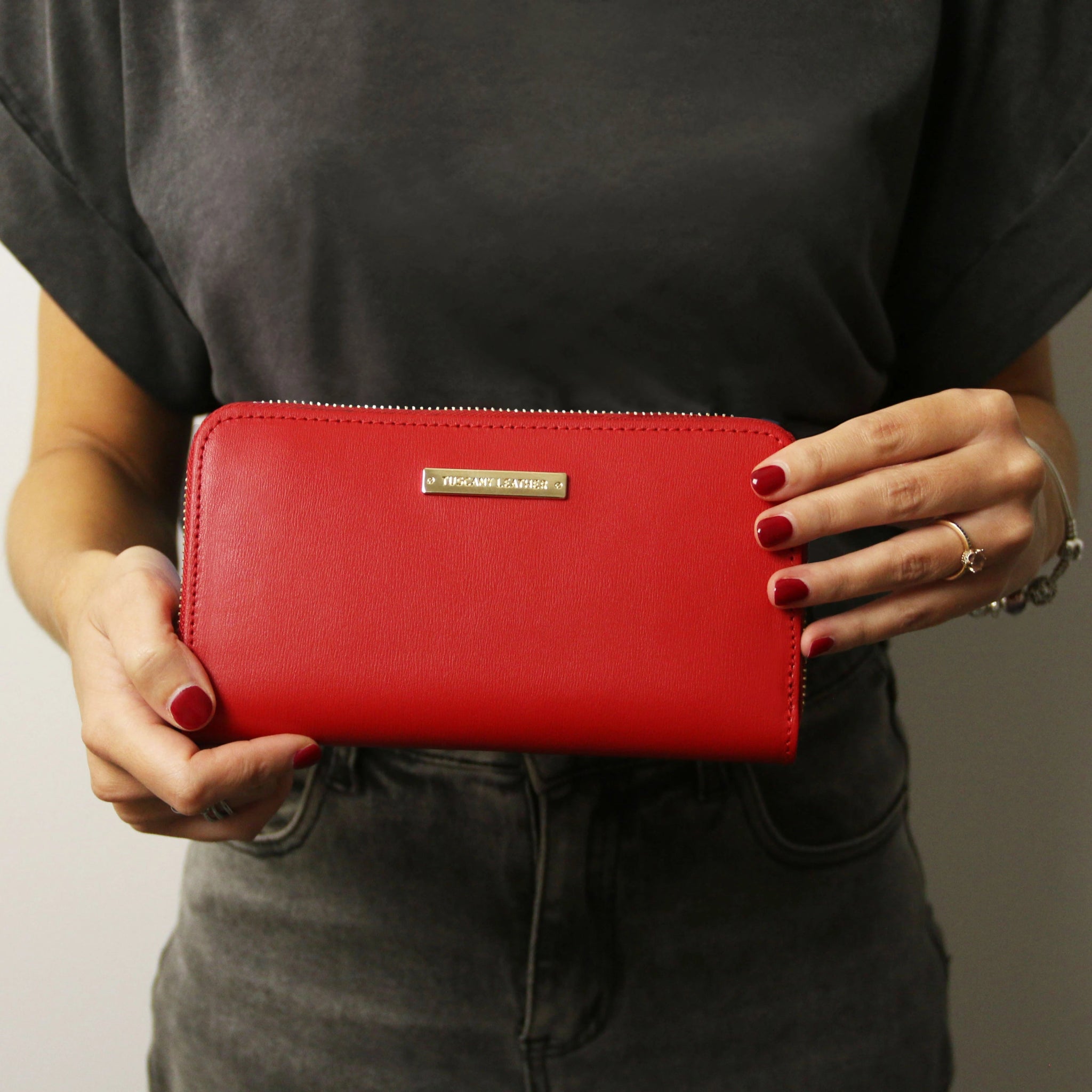 A model is holding the Ilizia Exclusive Zip Around Italian Leather Wallet in Lipstick Red