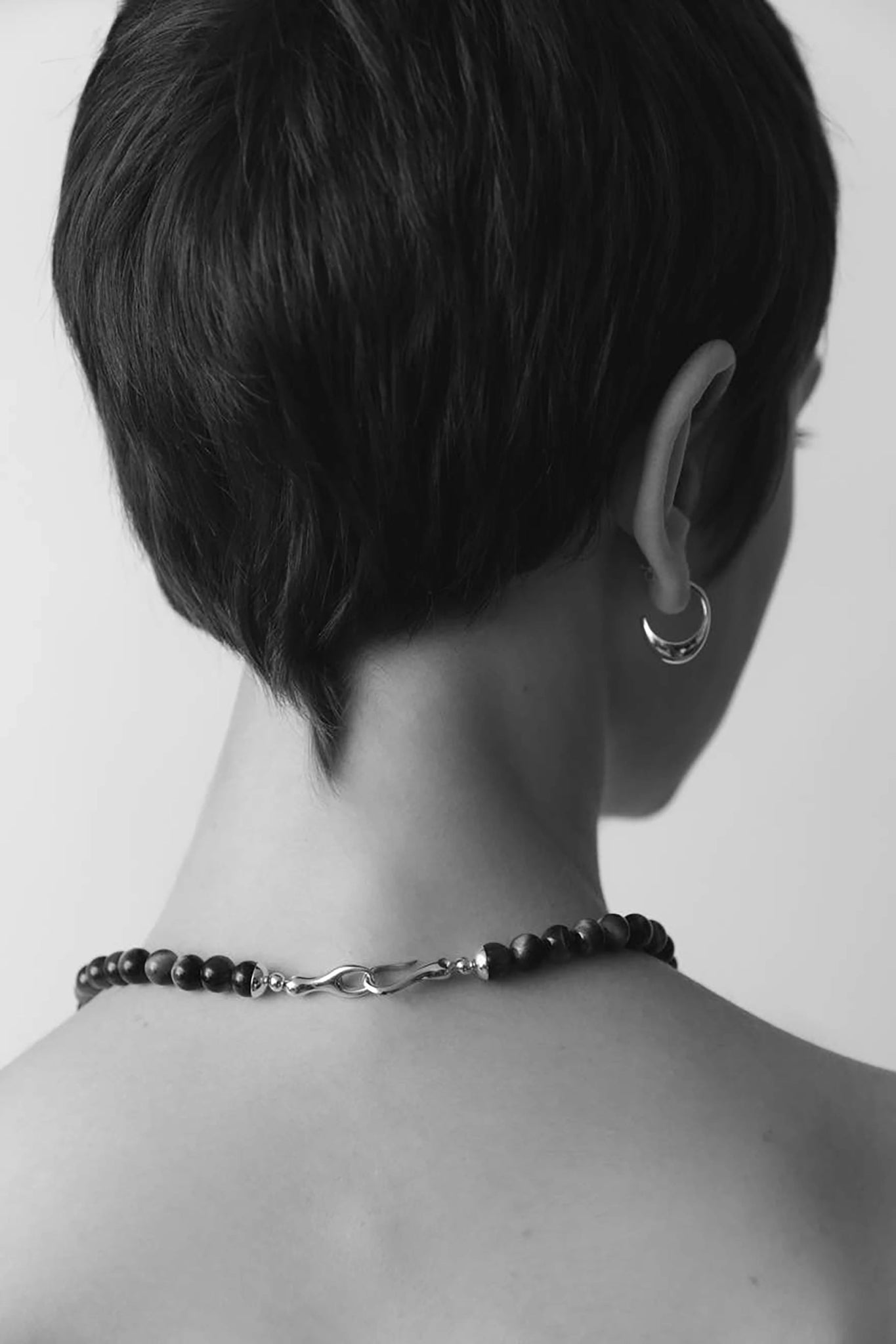 A model is wearing and presenting the Gold Hoop Earrings using a black and white photo taken behind her head so you can see the earring angle below the ear.