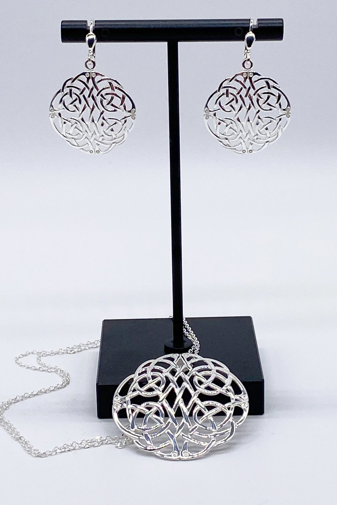 Irish Celtic Woven Knot Sterling Silver Earrings and necklace on a black jewelry stand against a warm gray background - L'Atelier Global