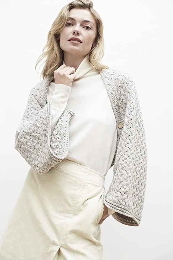 A female model wearing the Irish Clew Bay Supersoft Convertible Cape in oatmeal as a shrug showing the buttons closed under the arm
