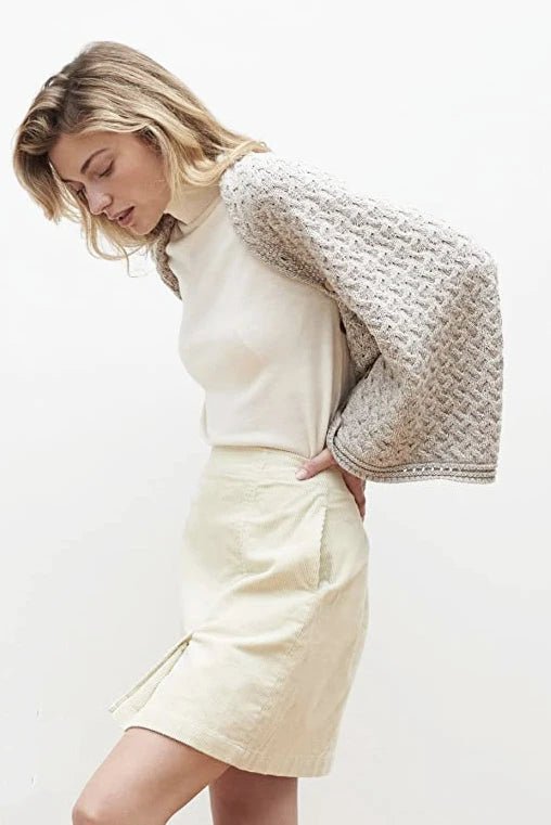 A female model wearing the Irish Clew Bay Supersoft Convertible Cape in oatmeal as a shrug