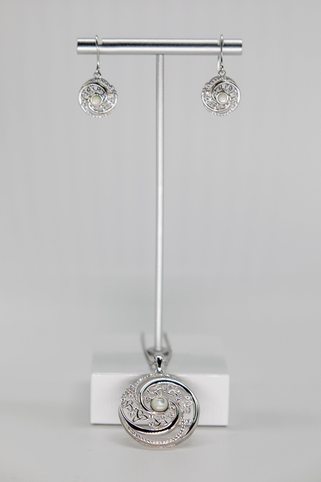 Irish Winter Solstice Swirl Mother of Pearl Earrings and necklace on a jewelry stand in front of a gray background