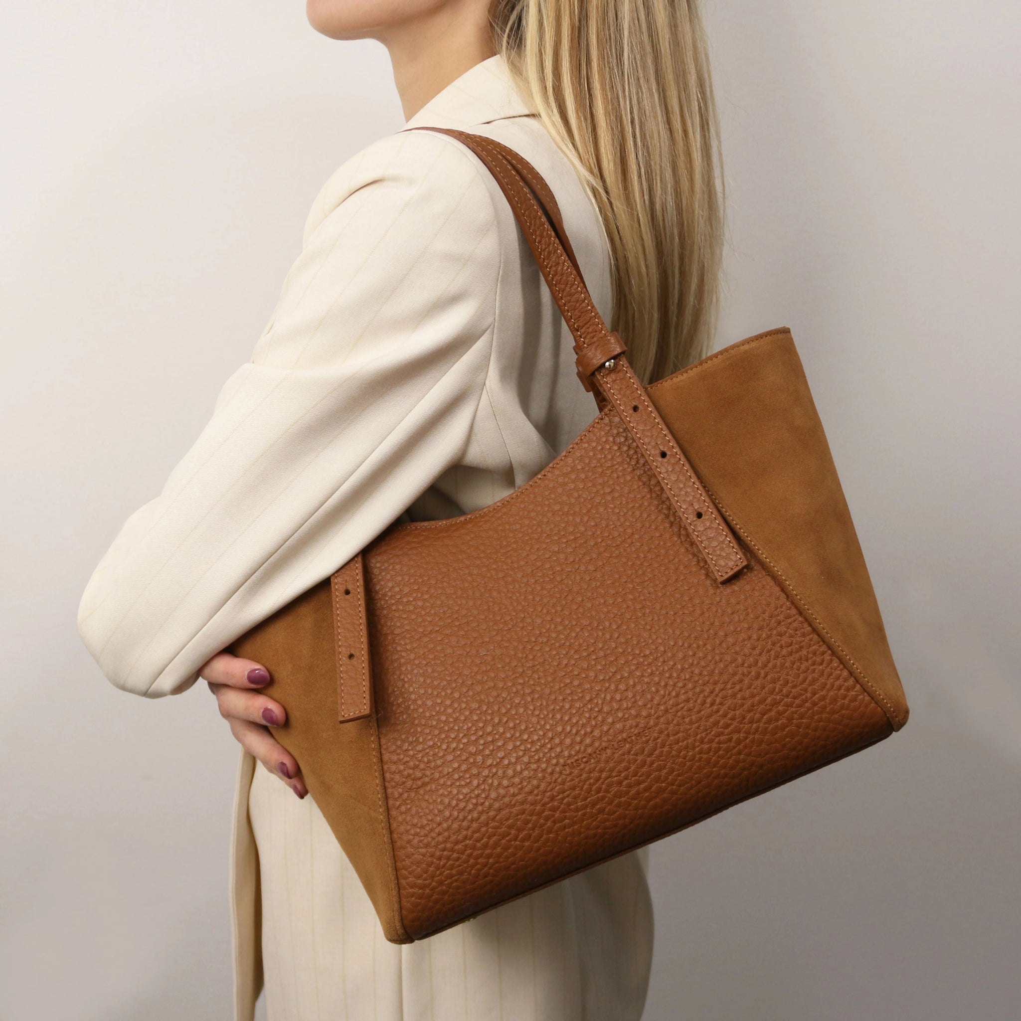 A woman is holding the Libra Leather Suede Shoulder Bag in cognac on her shoulder