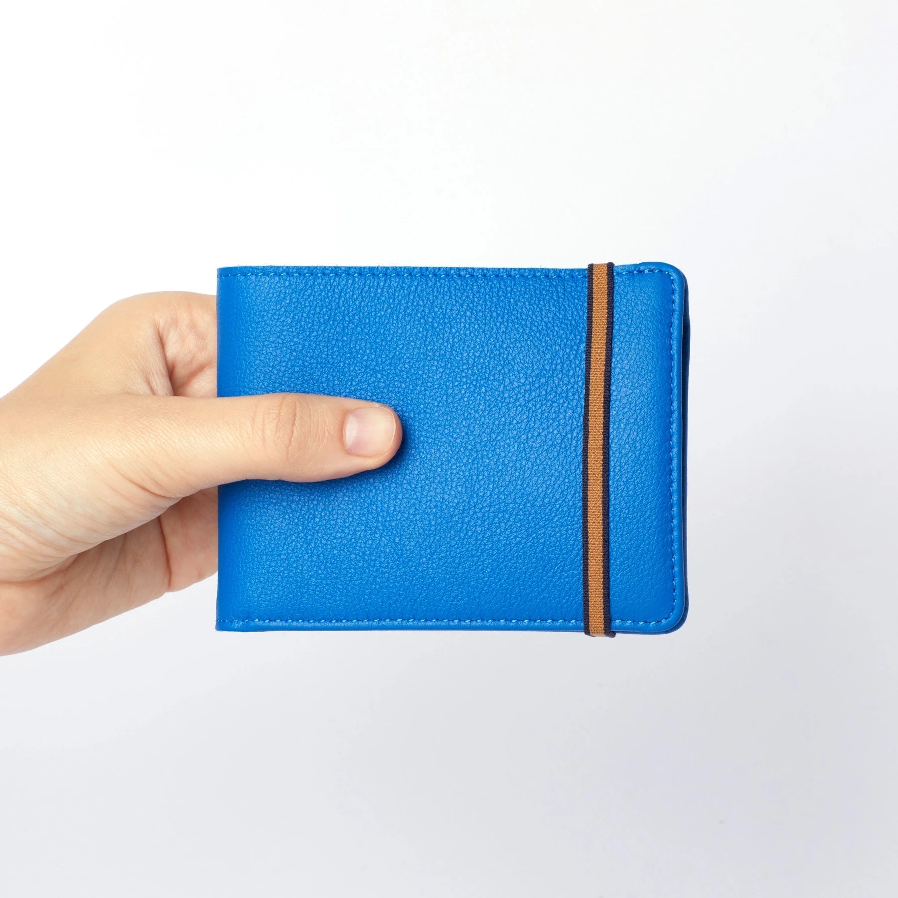 A hand is holding the Light Blue Minimalist Wallet with Coin Pocket showing gold and black elastic strap.
