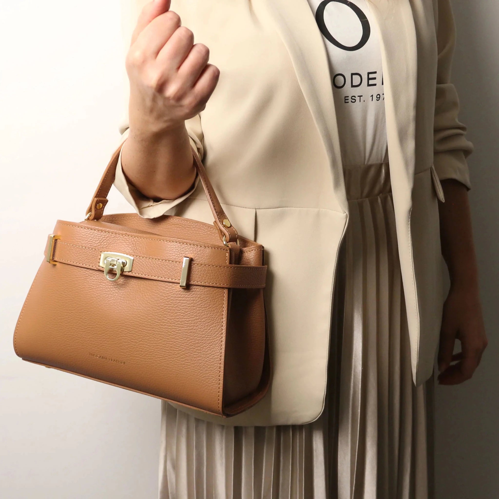 Woman wearing a beige suit jacket and skirt holding Maisy Italian Leather Tote Bag in caramel