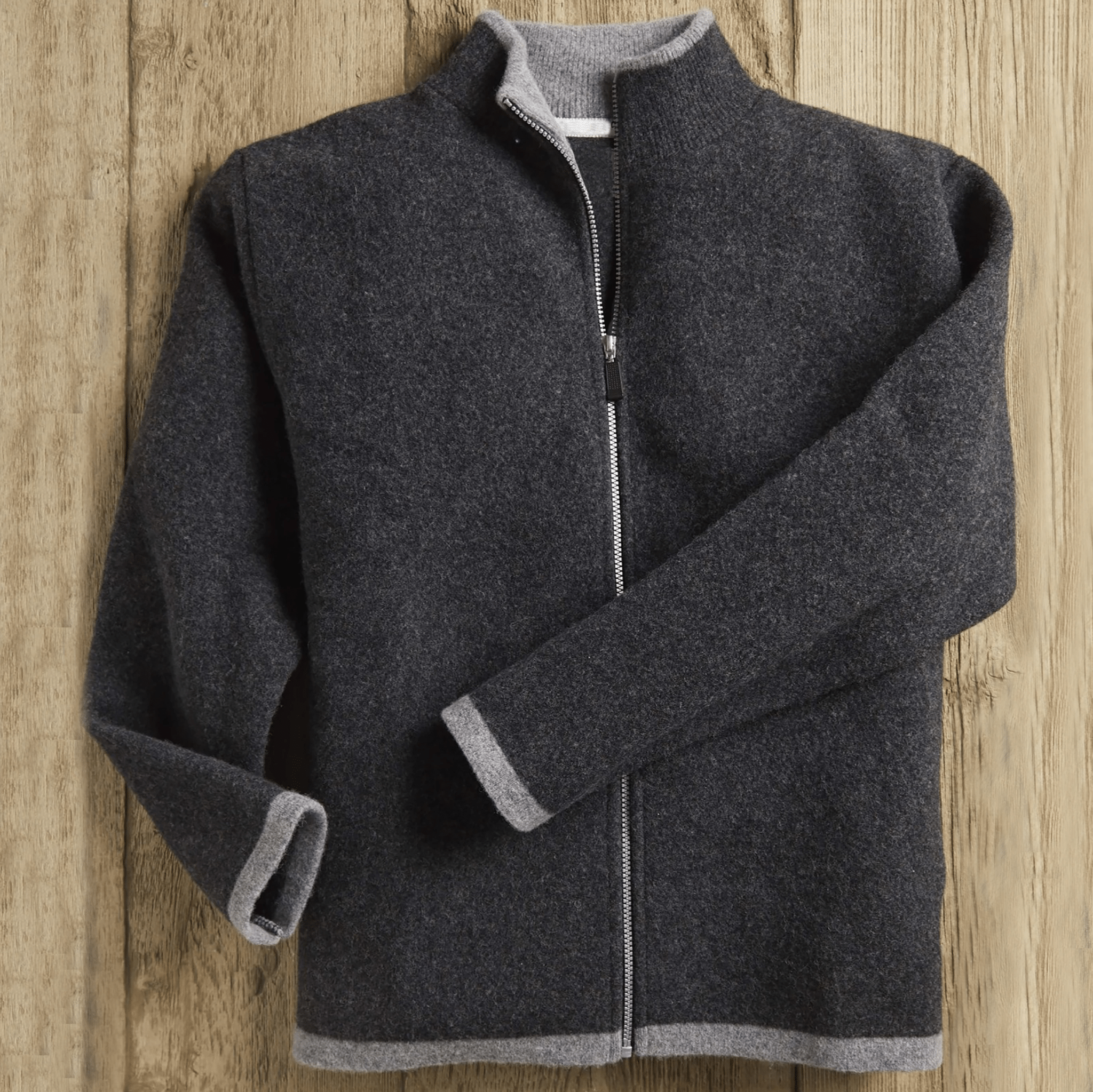Men's Scottish Borders Felted Wool Cardigan in Charcoal with zipper opened at upper chest, laying on a wood background