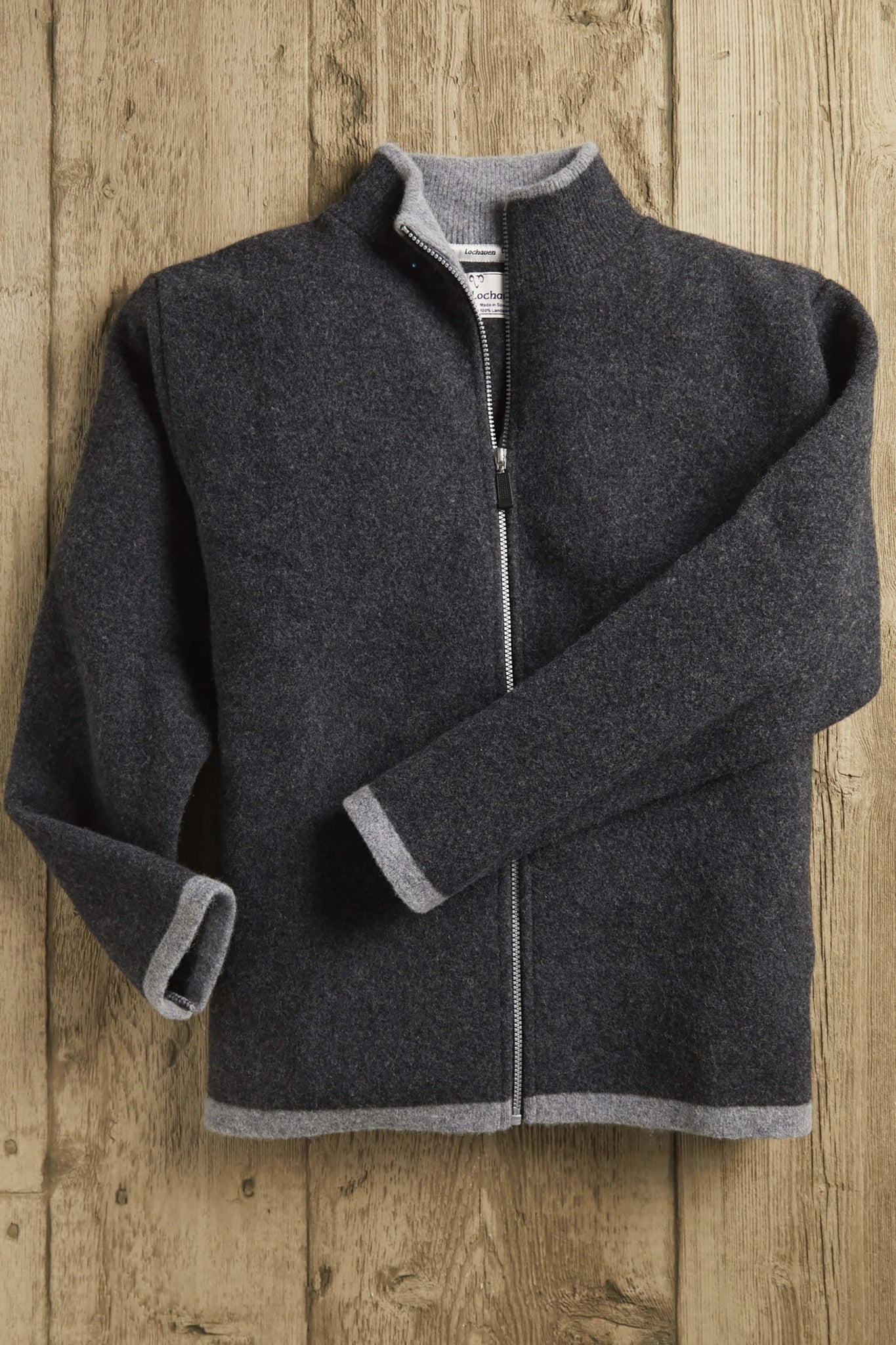 Men's Scottish Borders Felted Wool Cardigan in Charcoal with zipper opened at upper chest, laying on a wood background