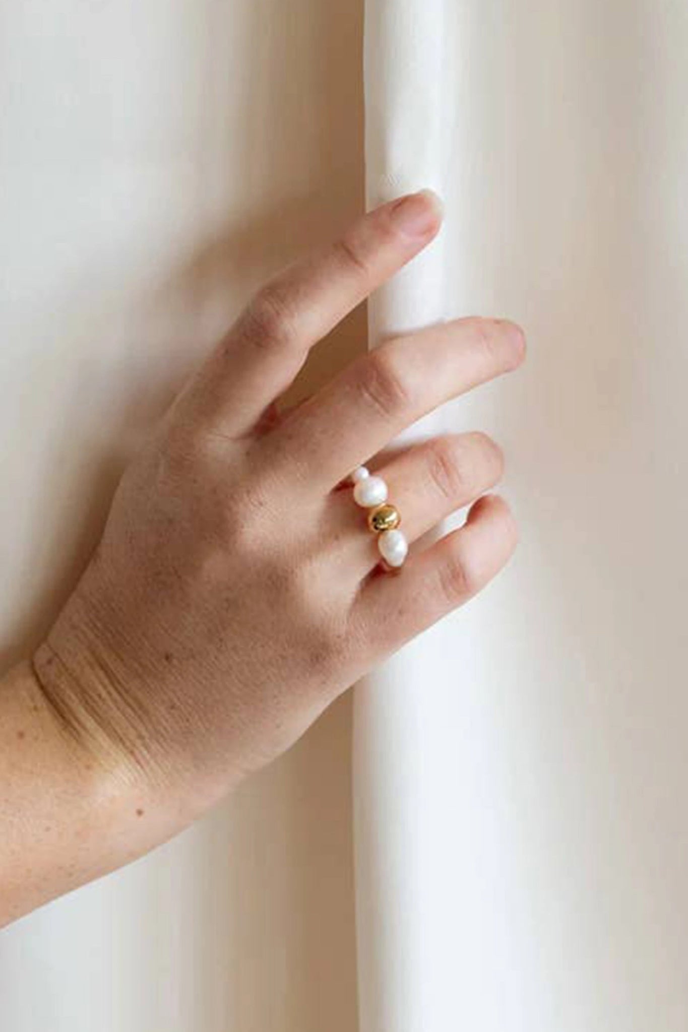 Menton Stretch Golden Pearl Ring on a hand with her hand placed on an ivory curtain - L'Atelier Global