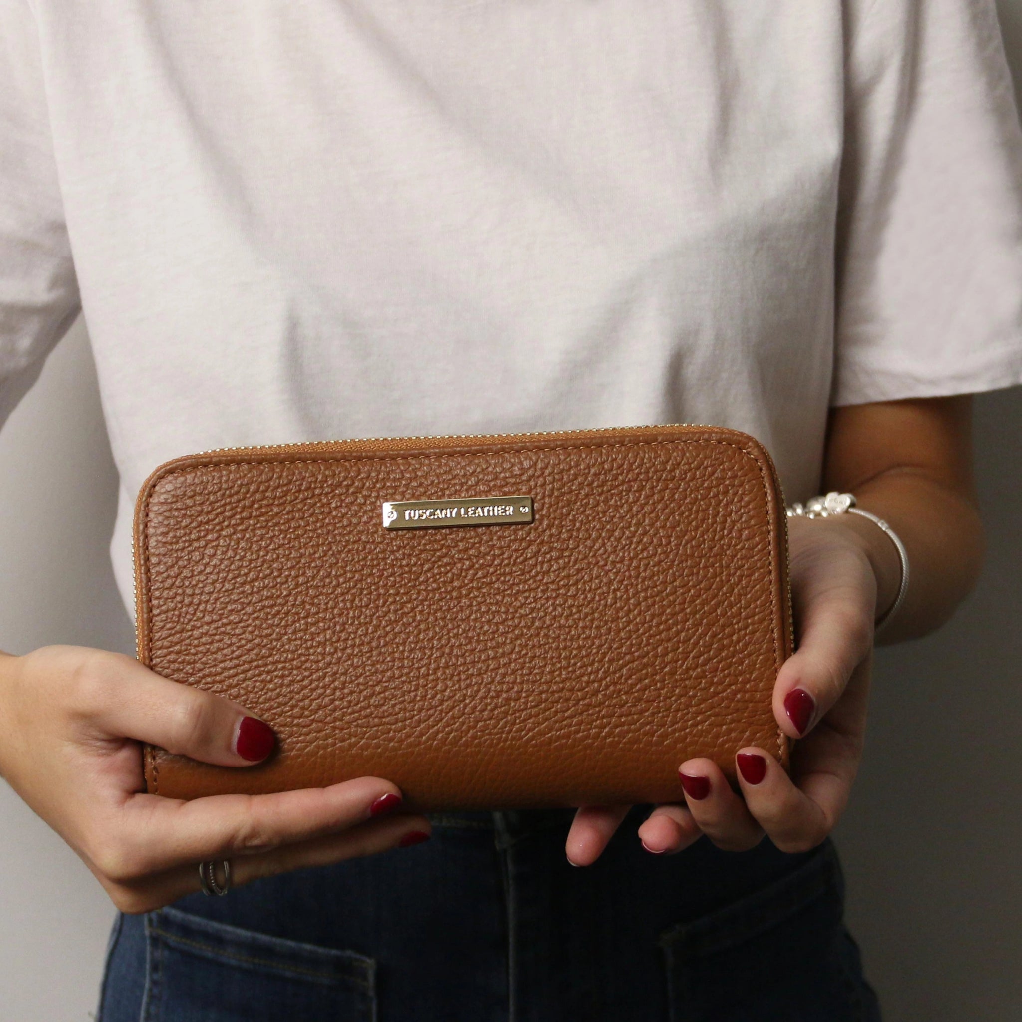 A model holding the Eris Exclusive Italian Leather Zip Around Wallet in Cognac