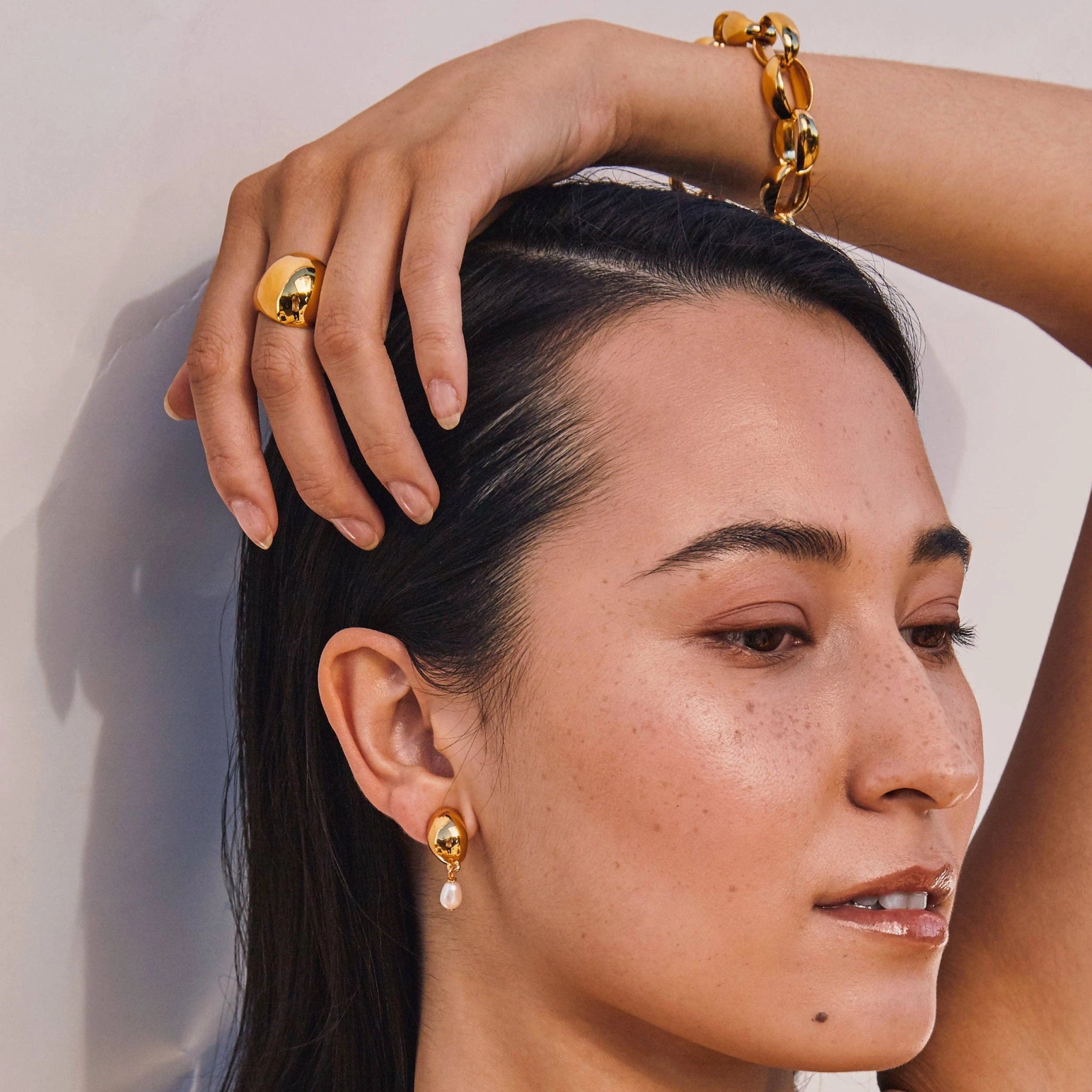 A model has her arm over her head wearing the Origin Chainlink Gold Bracelet .