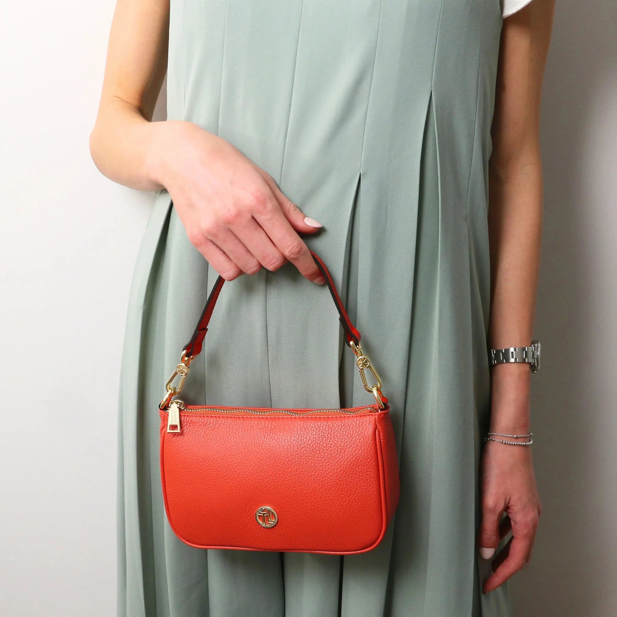 Woman carrying the Parfait Leather Clutch in coral with handle on white background