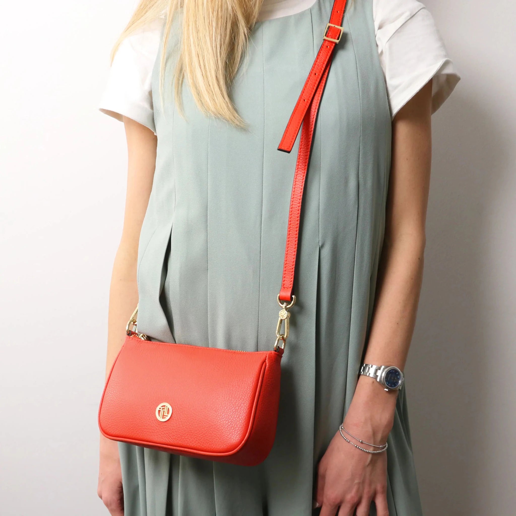 Woman carrying the Parfait Leather Clutch in coral with crossbody strap on white background