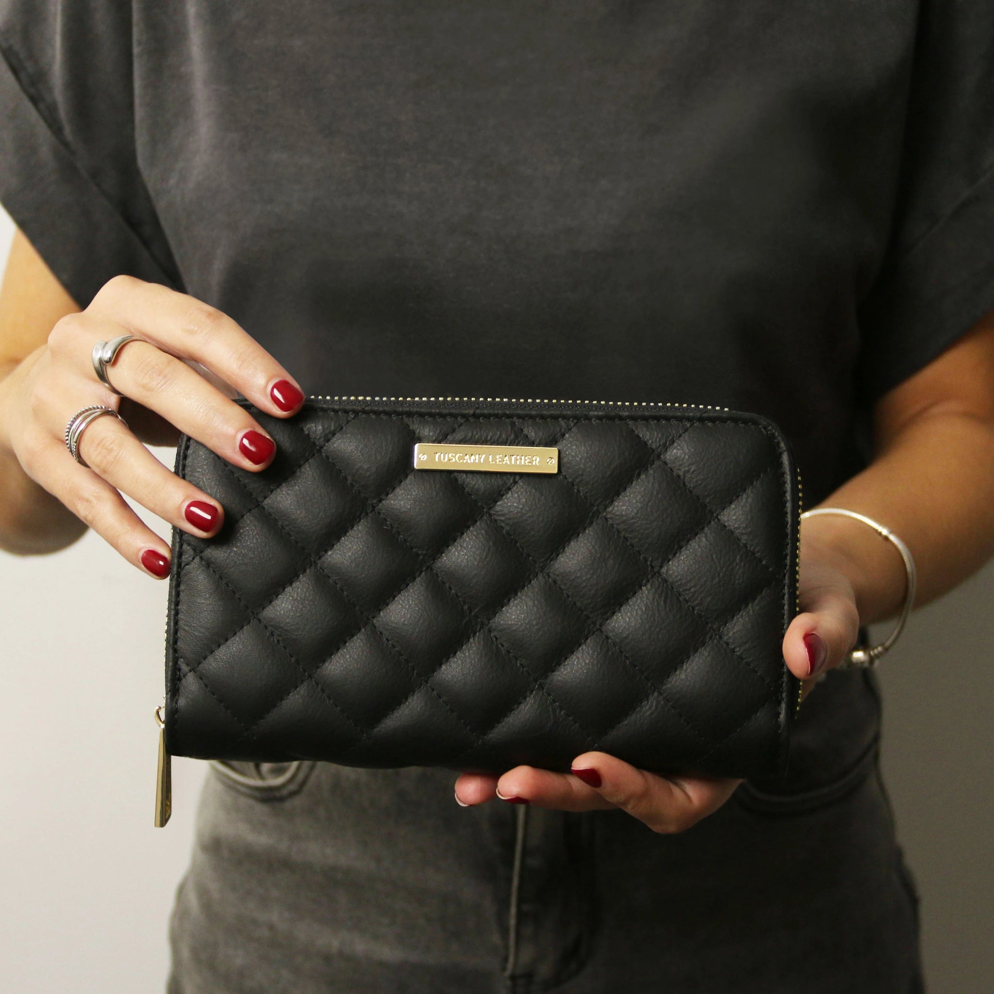A model is holding the Penelope Exclusive Zip Around Italian Leather Wallet in Black