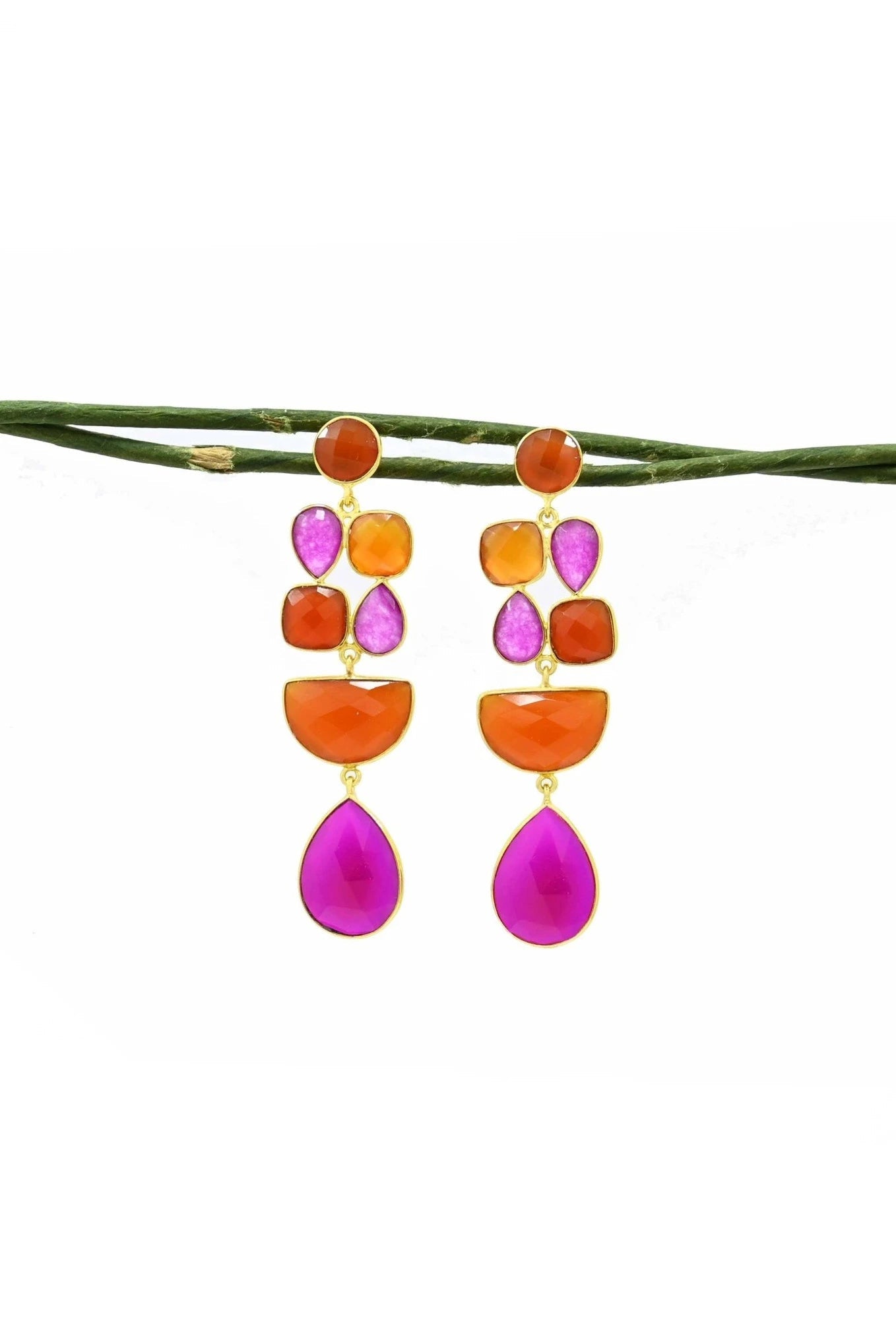 Colorful earrings in pink and orange gemstones hanging from green branch