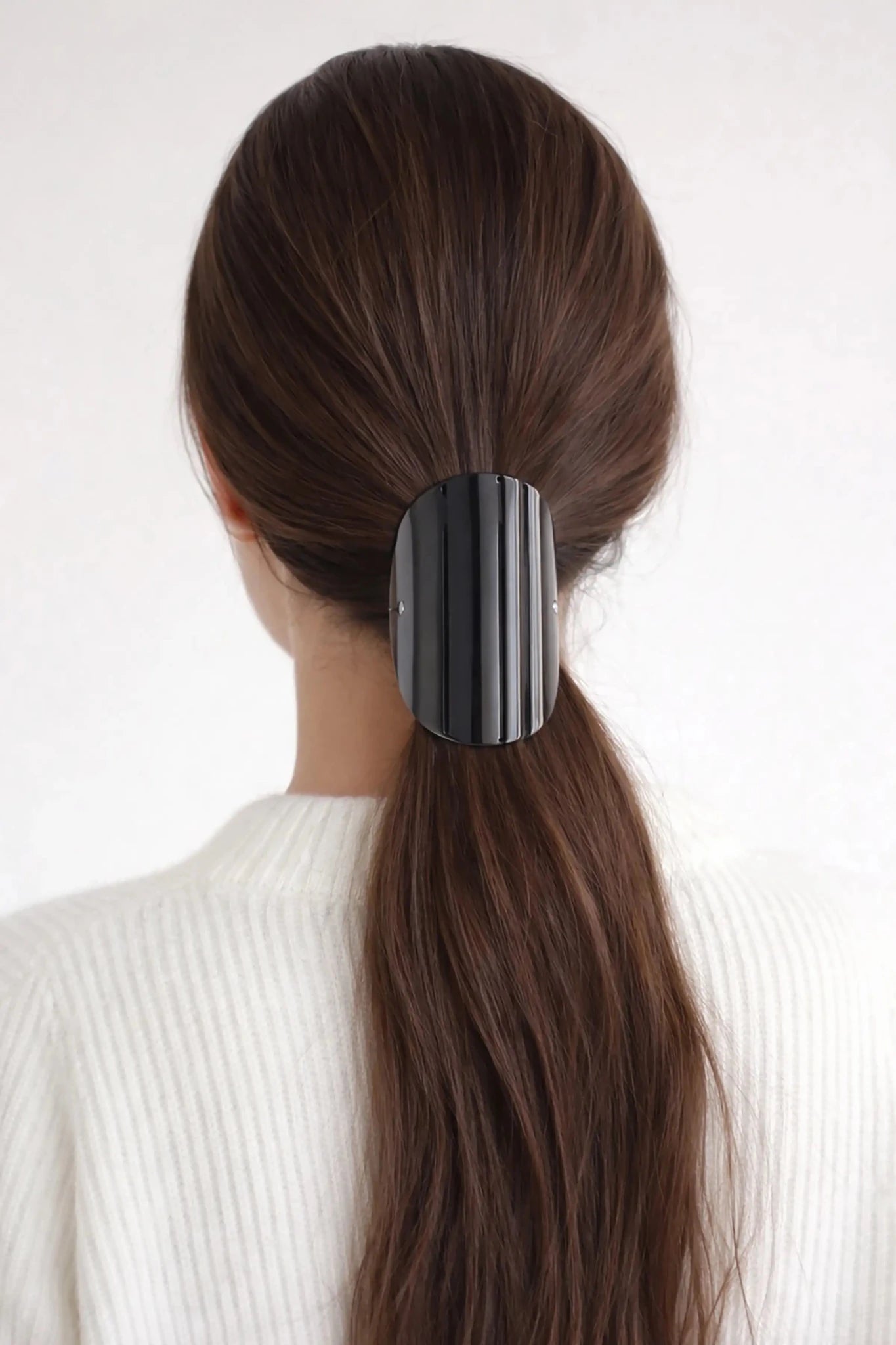 Woman with brunette long hair wearing the Sculpted Arc Barrette in her ponytail against a white background