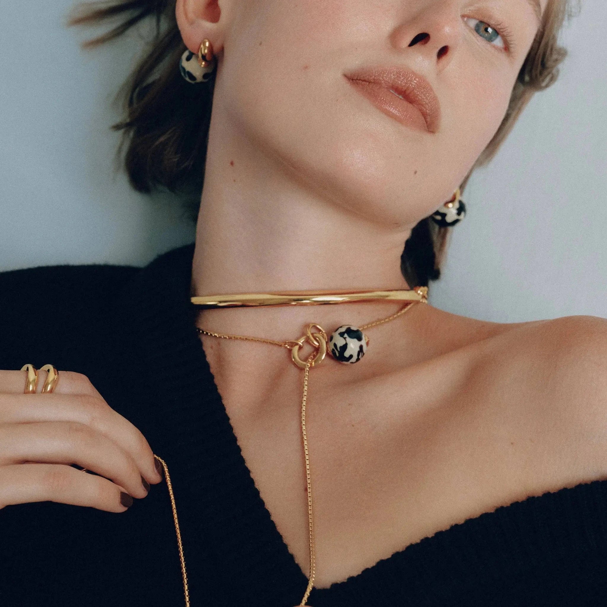 Close-up of woman wearing gold jewelry and Arc Collar on a neutral background