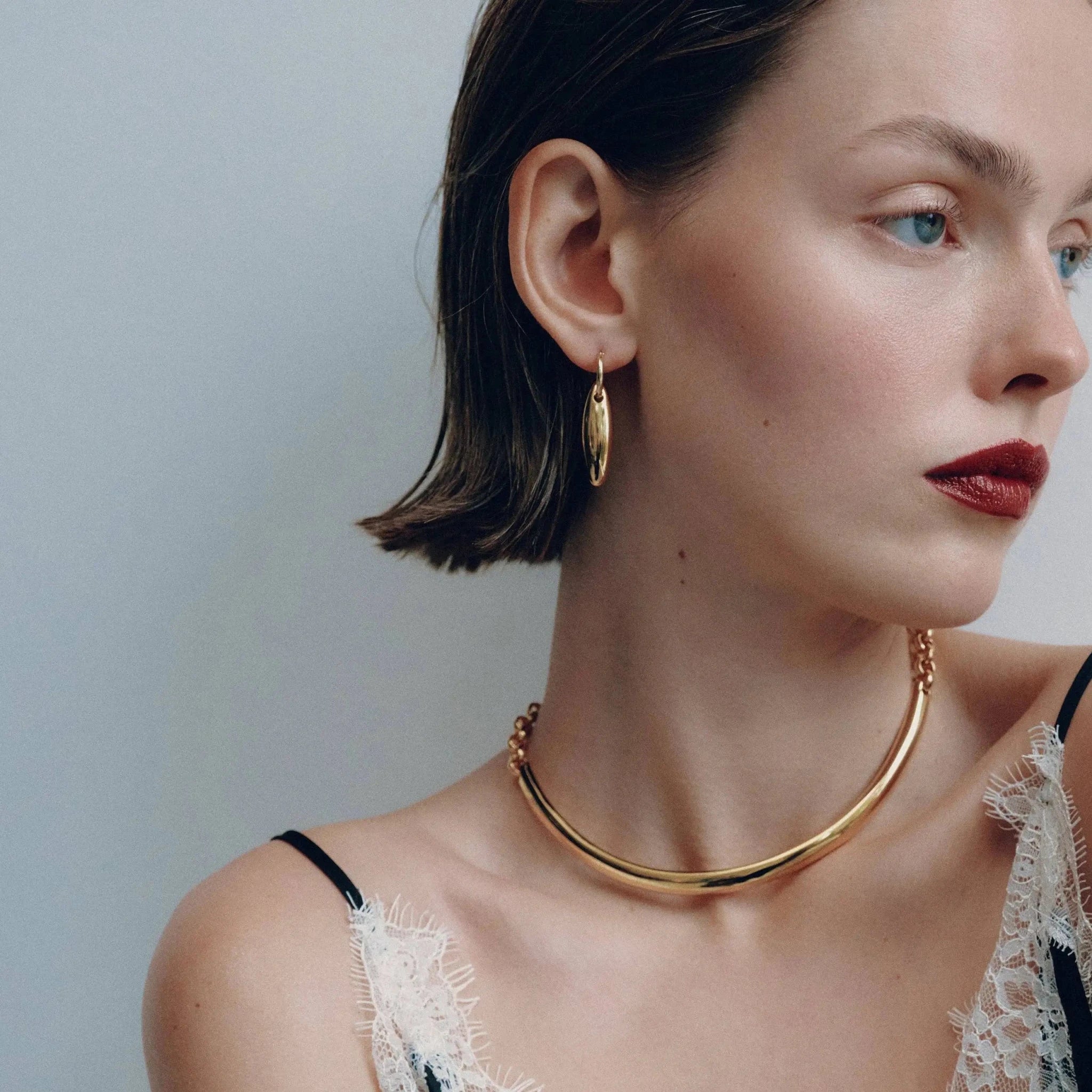 Woman wearing the Golden Arc Collar gold necklace and hoop earrings against a neutral background