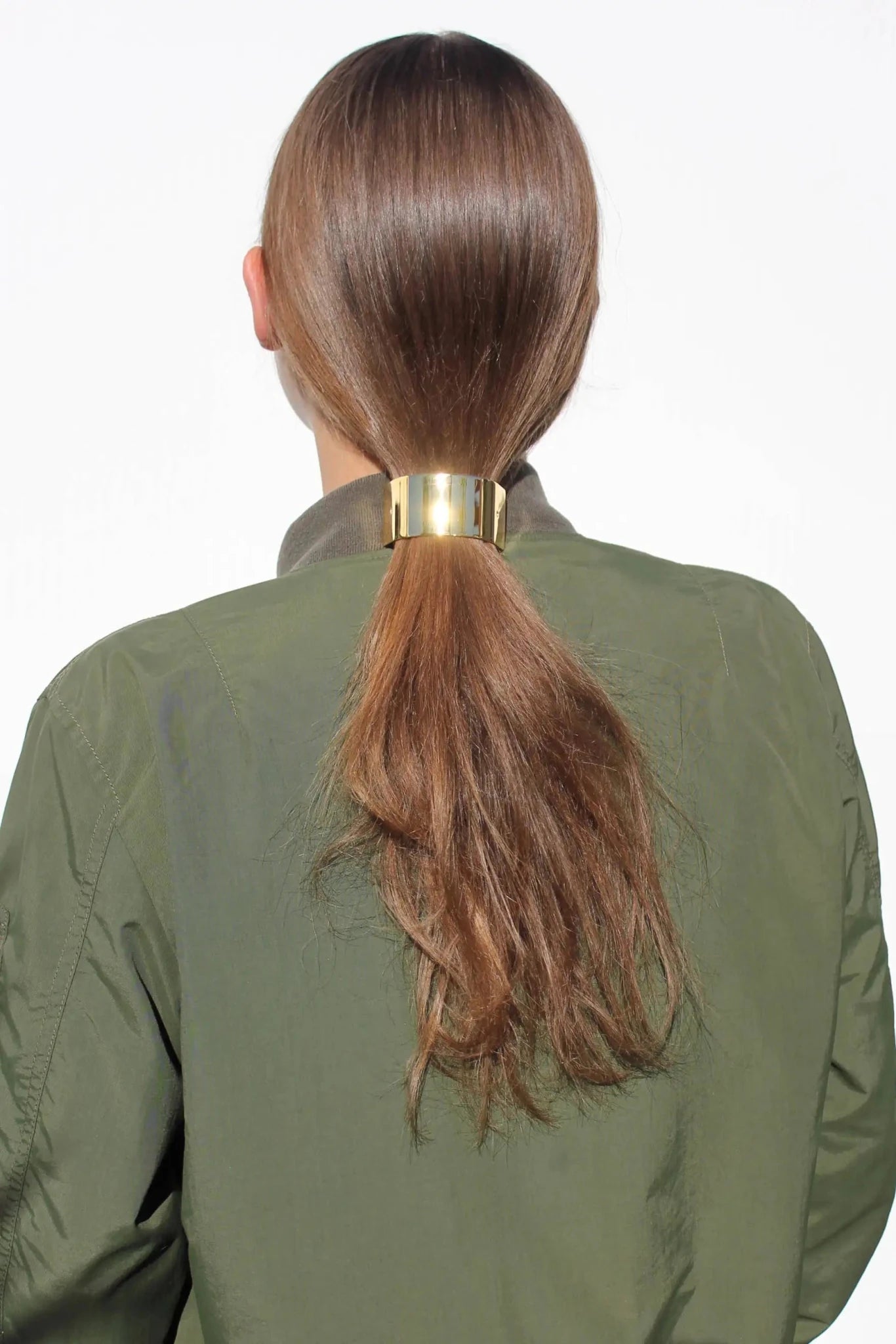 Woman with brown hair tied in a ponytail wearing a gold barrette on a white background