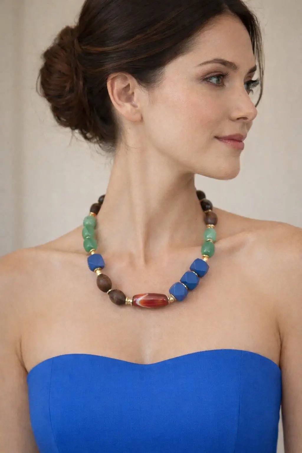 Woman wearing the Sunset Over Cartagena Gold Beaded necklace with a blue top against a neutral background