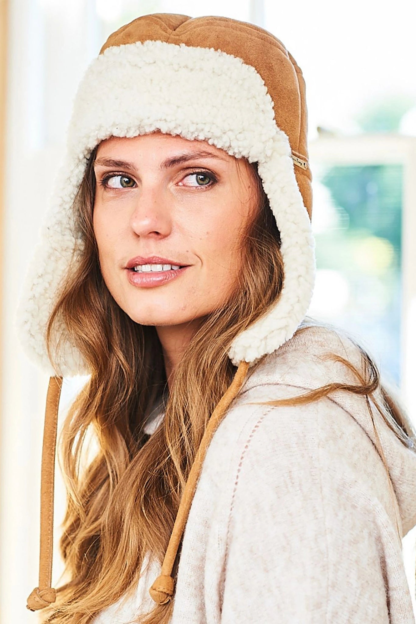 Side view Tie Trapper Sheepskin Ear Flap Hat in Brand Cream on a model, ear flaps down