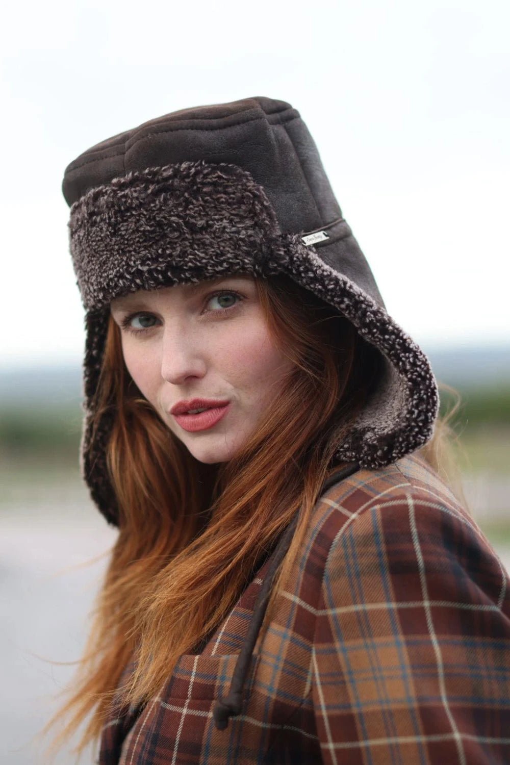 Tie Trapper Sheepskin Ear Flap Hat in Dark Brown on a female model, front side angled view, ear flaps down