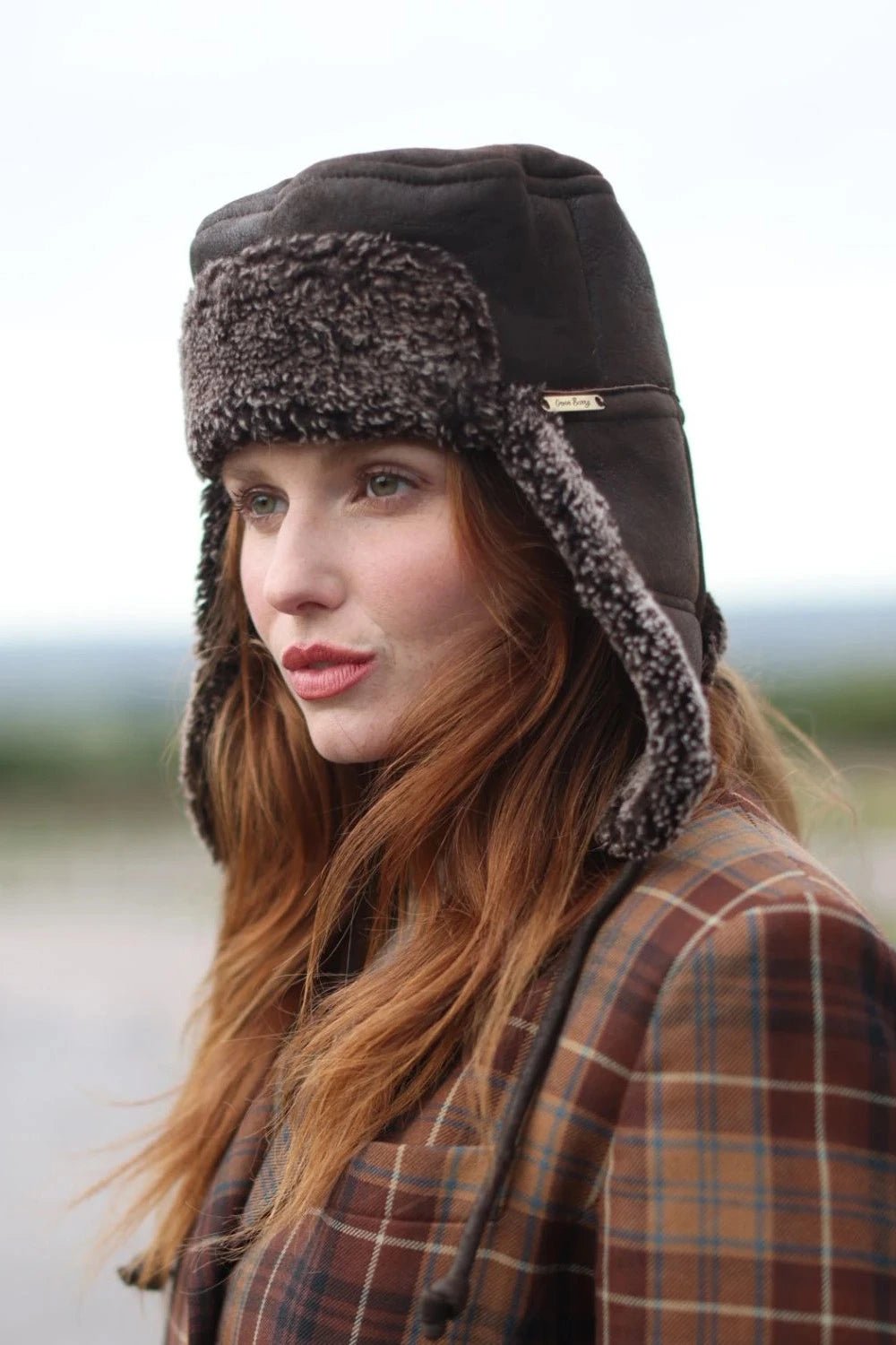 Tie Trapper Sheepskin Ear Flap Hat in Dark Brown on a female model, side view ear flaps down
