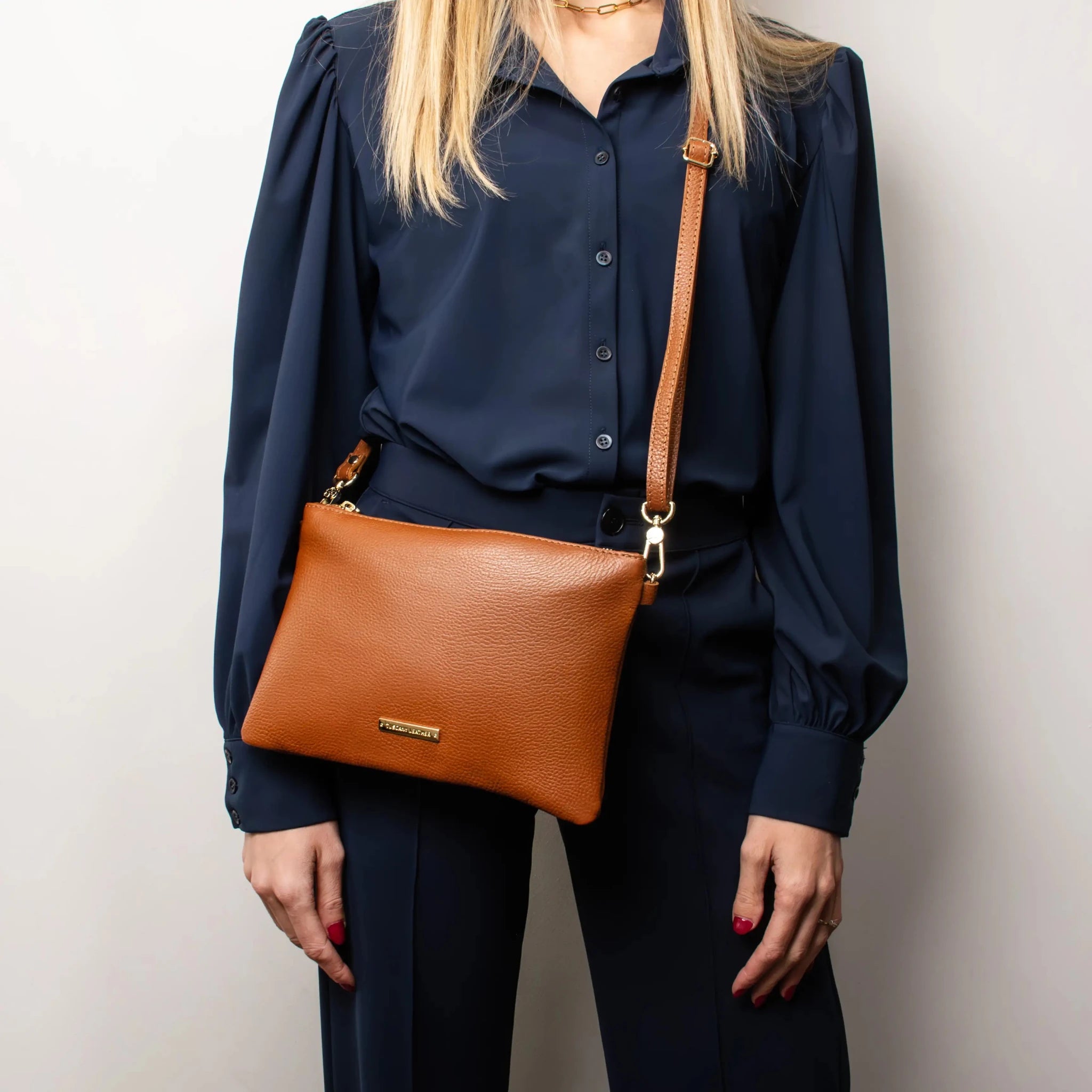 Woman wearing navy clothing, carrying Leather Clutch in Cognac as a cross body