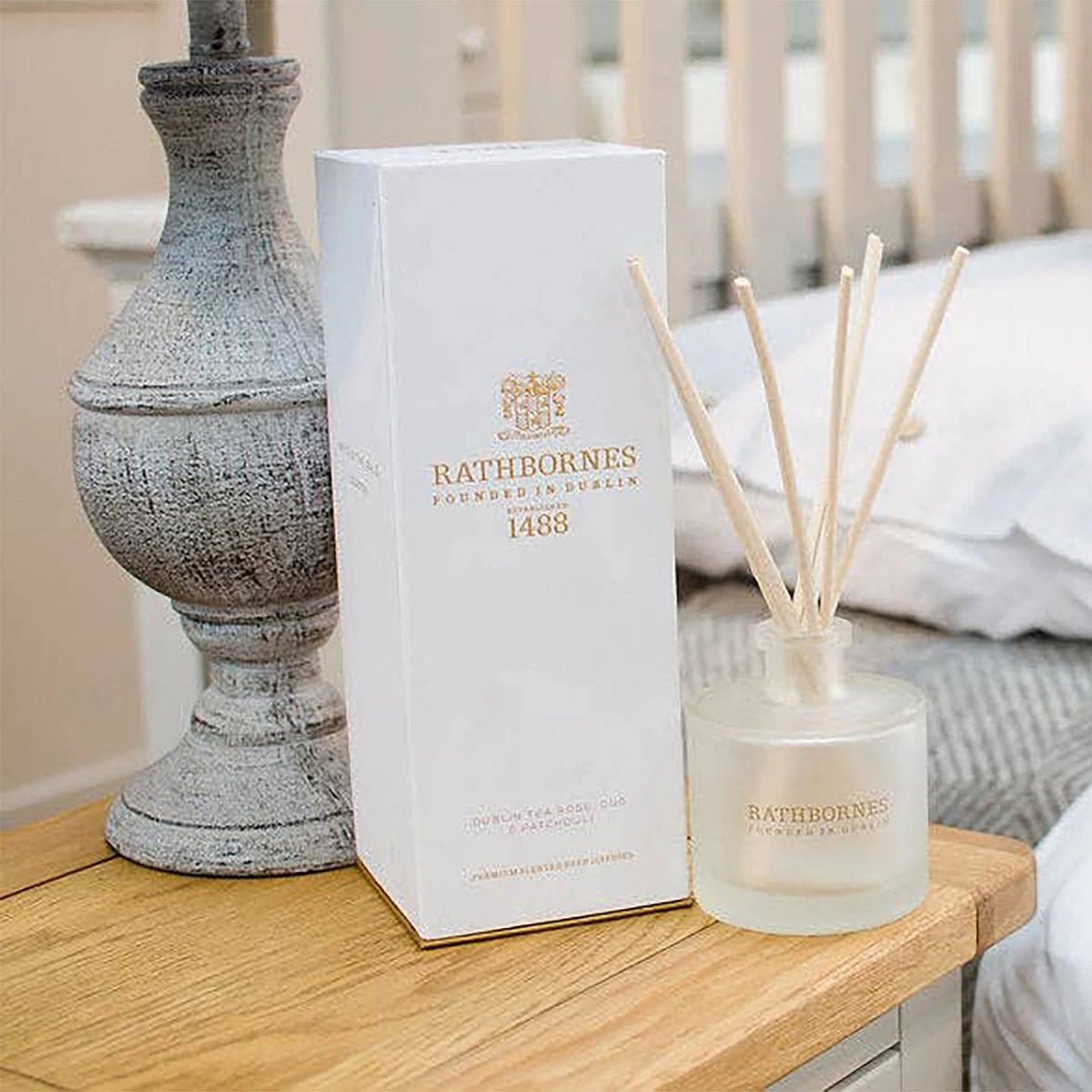 Wild Mint, Watercress & Thyme Scented Reed Diffuser white bottle and shipping box on a bedroom table