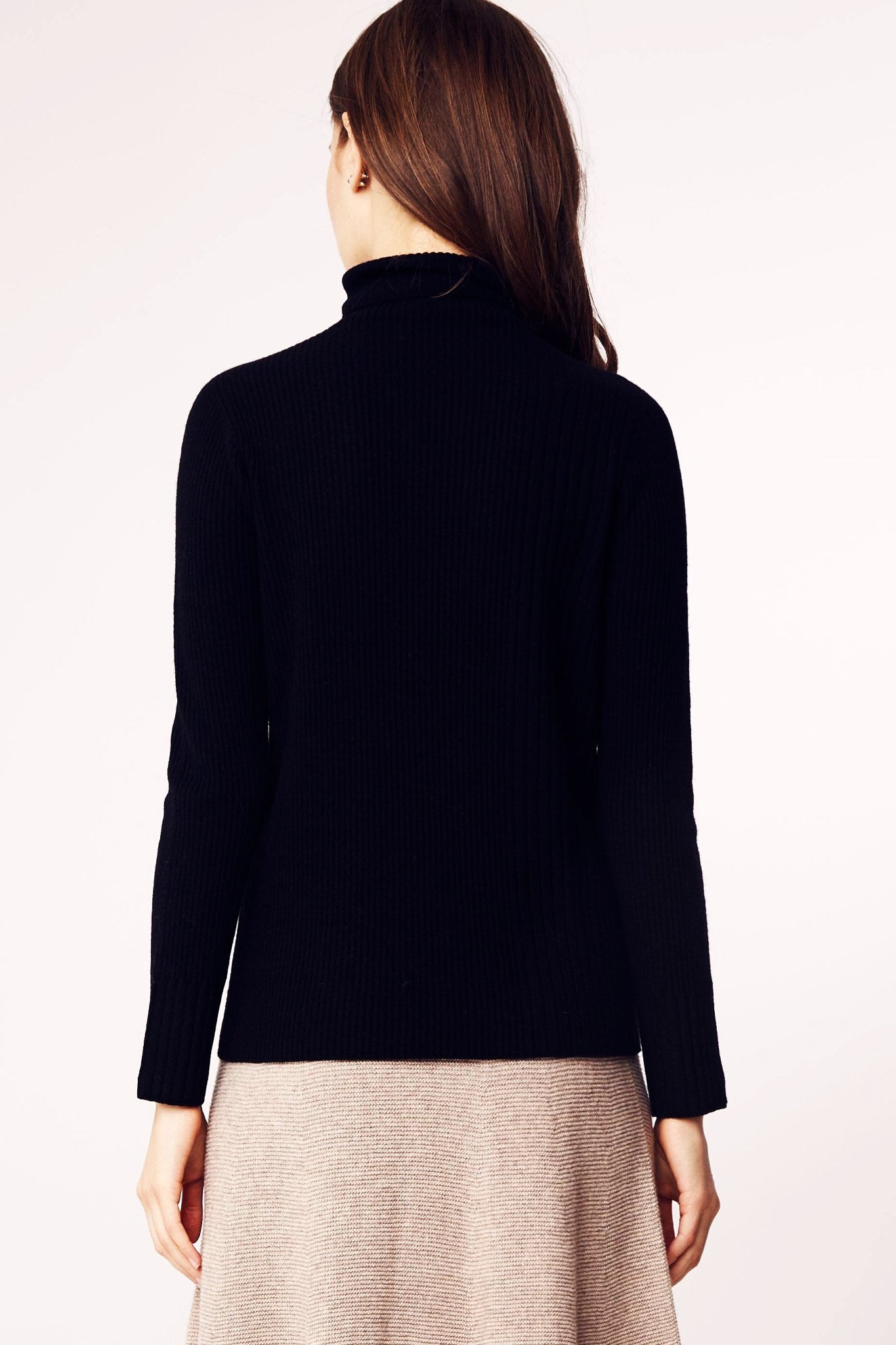 Model is standing and wearing the Seamless Ribbed Classic Turtleneck Sweater in Black on a khaki mid length skirt