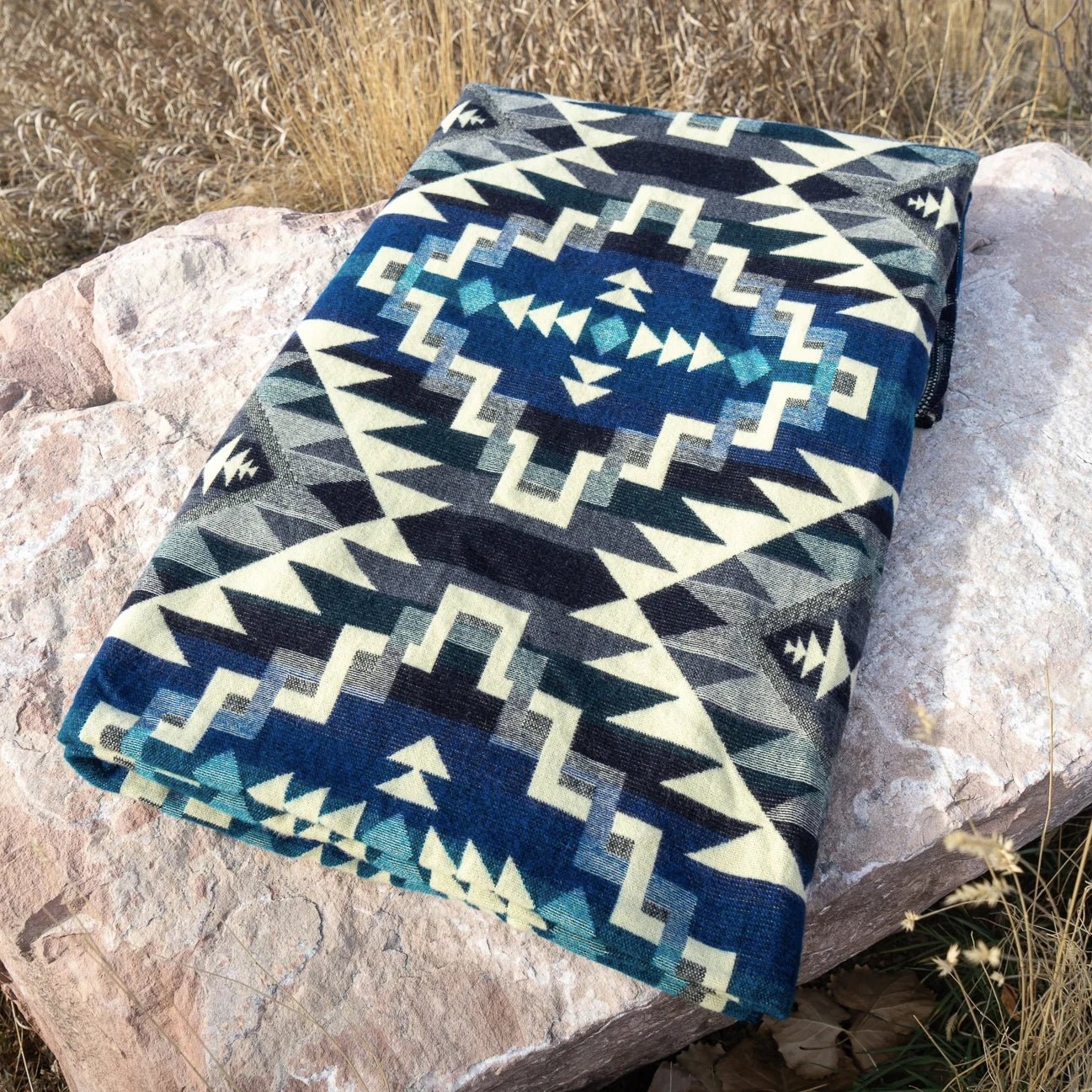 Andean Blue Chakana Alpaca Wool Blanket folded and laying no large rock - L'Atelier Global