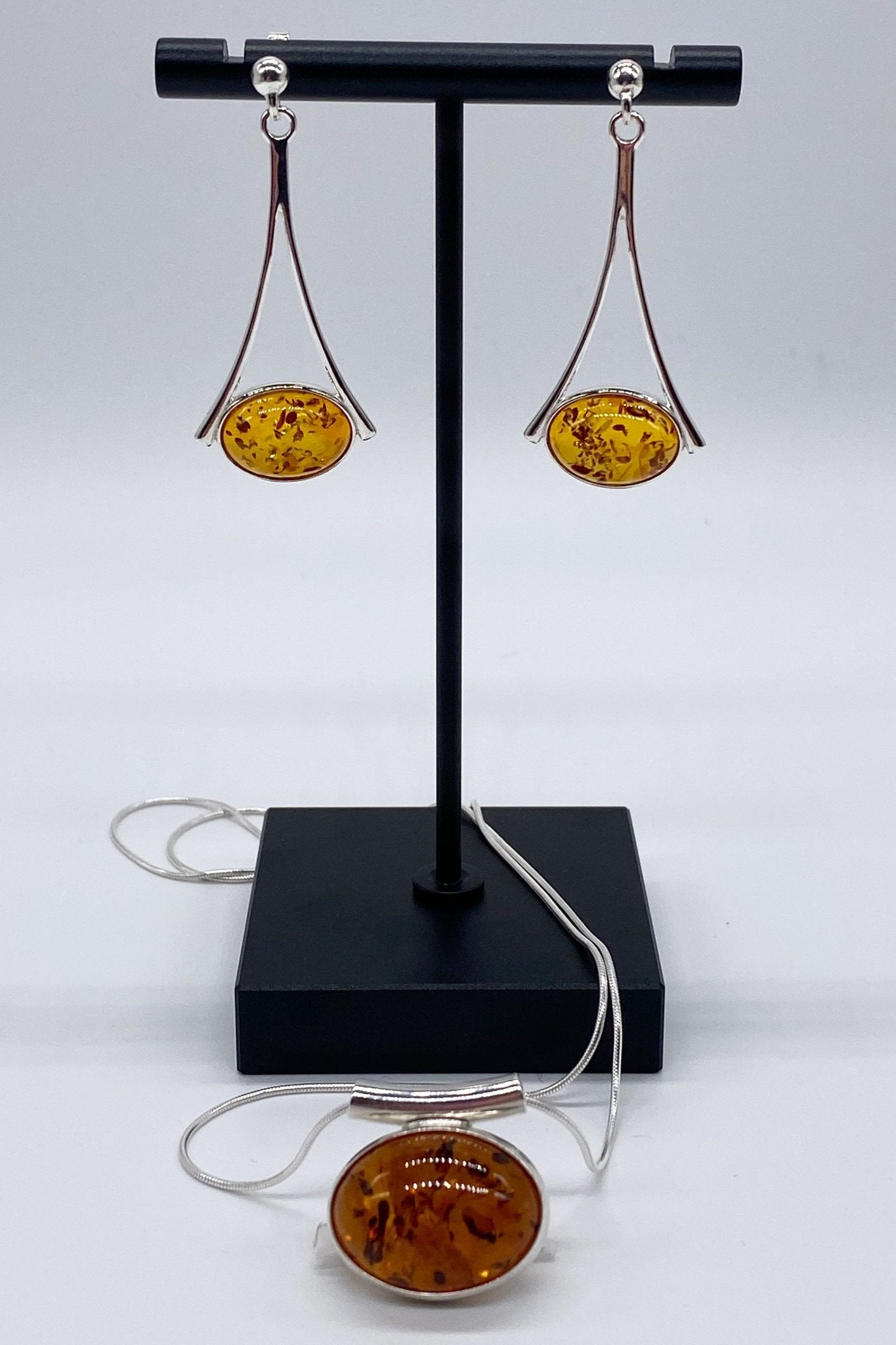 Baltic Honey Amber Slide Pendant Necklace and earrings are presented on a black jewelry stand. The dangle earrings are hanging while the pendant is laying in front of the stand and its chain wrapping around the stand base.