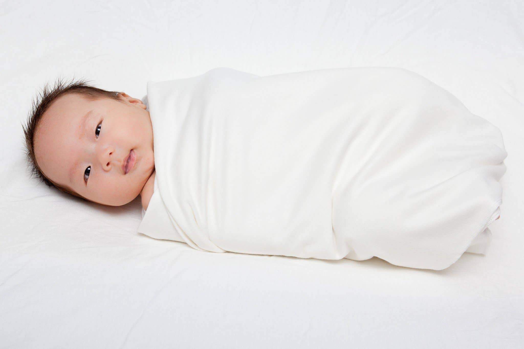 A baby is swadled by the Bamboo Swaddle Blanket in white