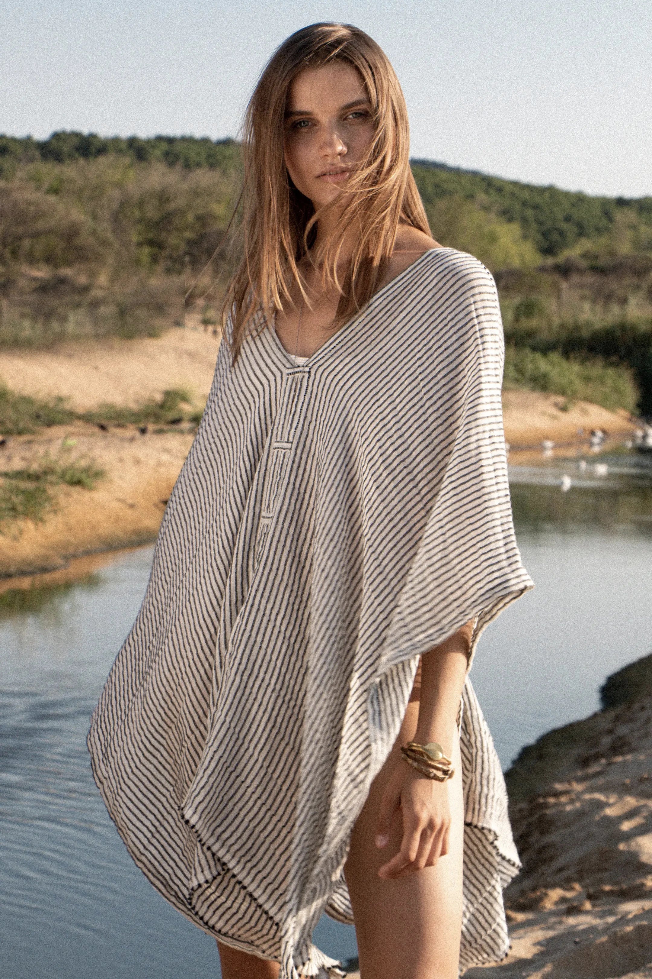 A female model is wearing the Beach Day Black Striped Kimono by a creek