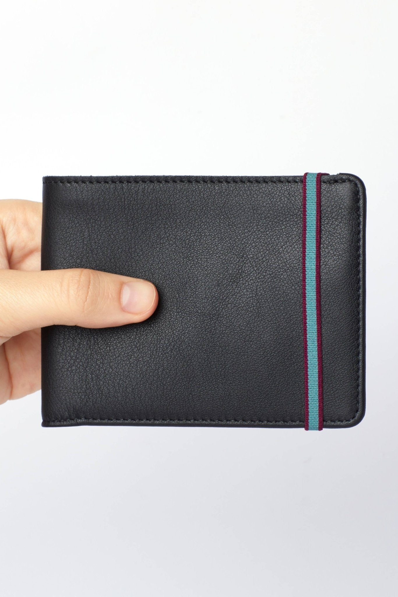 A man's hand holding the Black Minimalist Wallet with a blue elastic closure on a white background - L'Atelier Global