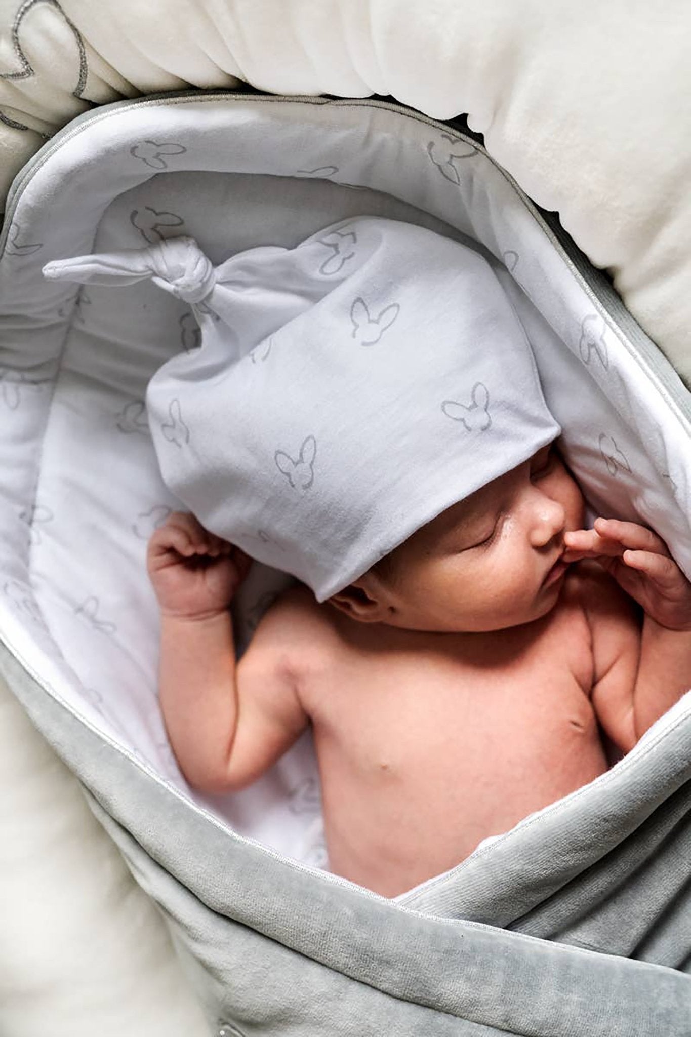 A baby is laying in the Blue Velvet Wrapping Cape wearing the Beanie - L'Atelier Global