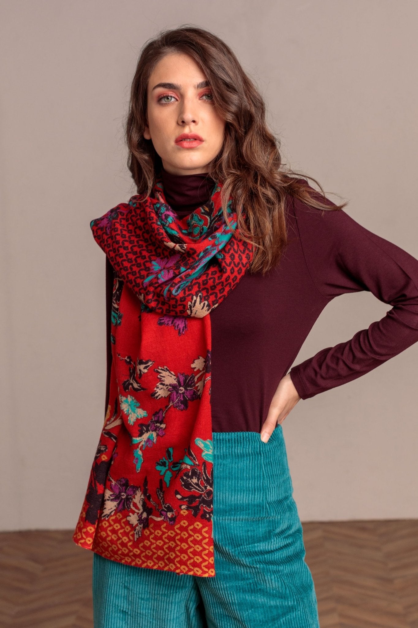 Botanical Garden Serbian Merino Wool Shawl in Red on a female model wearing a burgundy sweater and jeans with her left hand on her hip