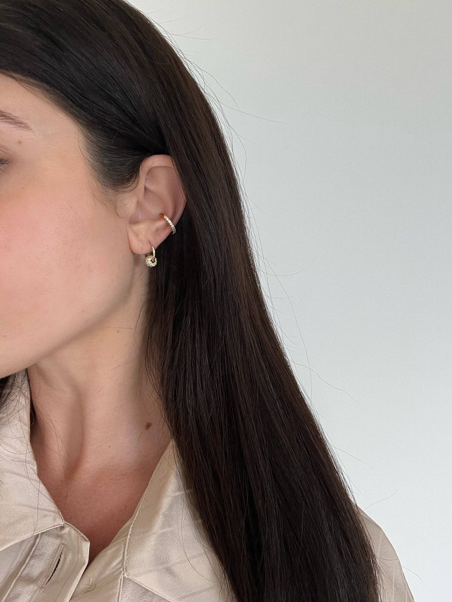 Brasilia Golden Huggie Earrings on a model with long dark brown hair. She s showing her right ear.