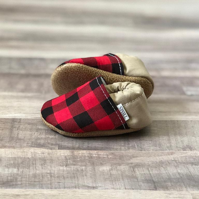 Buffalo Plaid And Tan Moccasins showing outsoles on a soft ash hued wood table