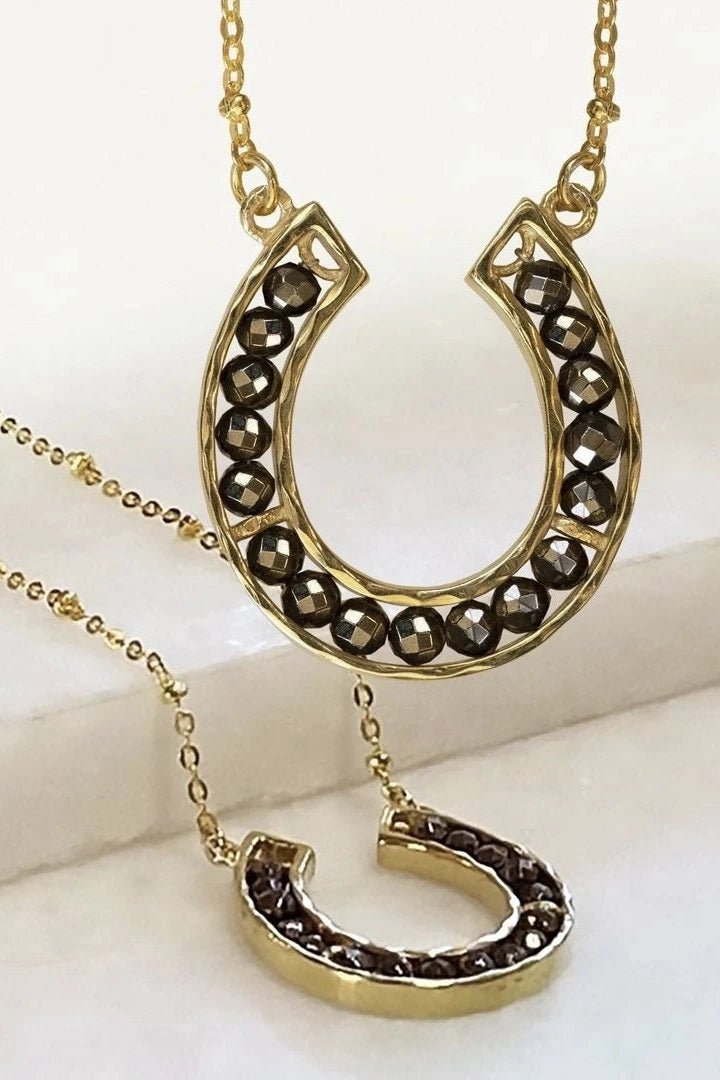 Capriole Horseshoe Gold Necklaces, one hanging and one is laying below showing the thickness of the width.