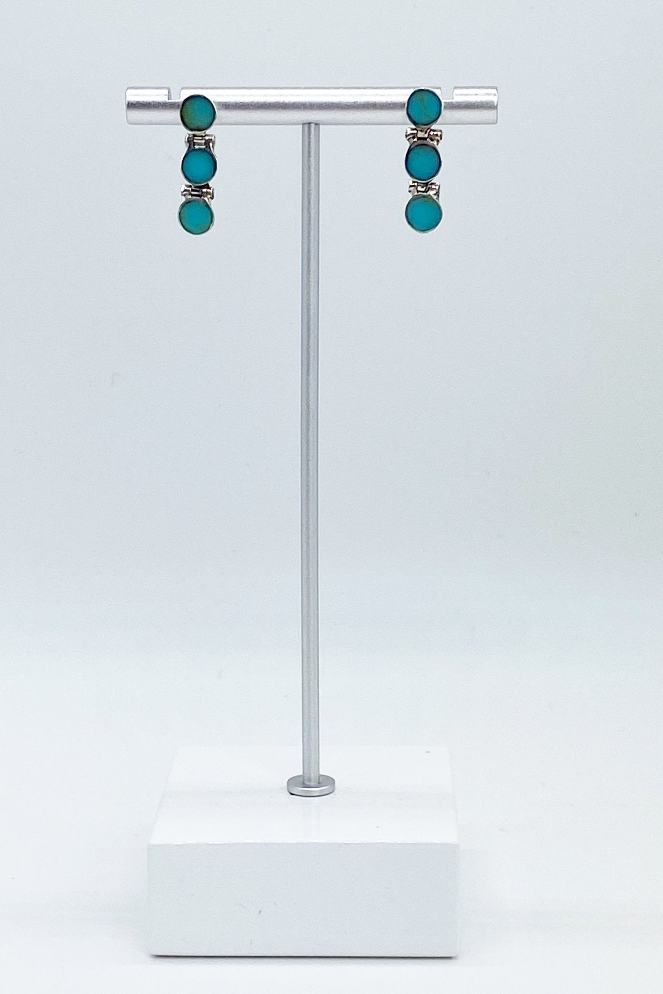 Chilean Turquoise Round Drop Earrings hanging on a jewelry stand with a white marble base - L'Atelier Global