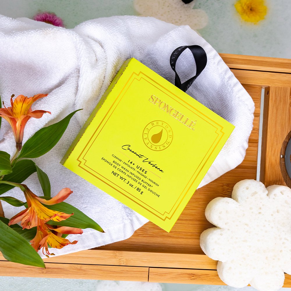 Coconut Verbena Flower Spa Body Buffer yellow box resting on a white towel.