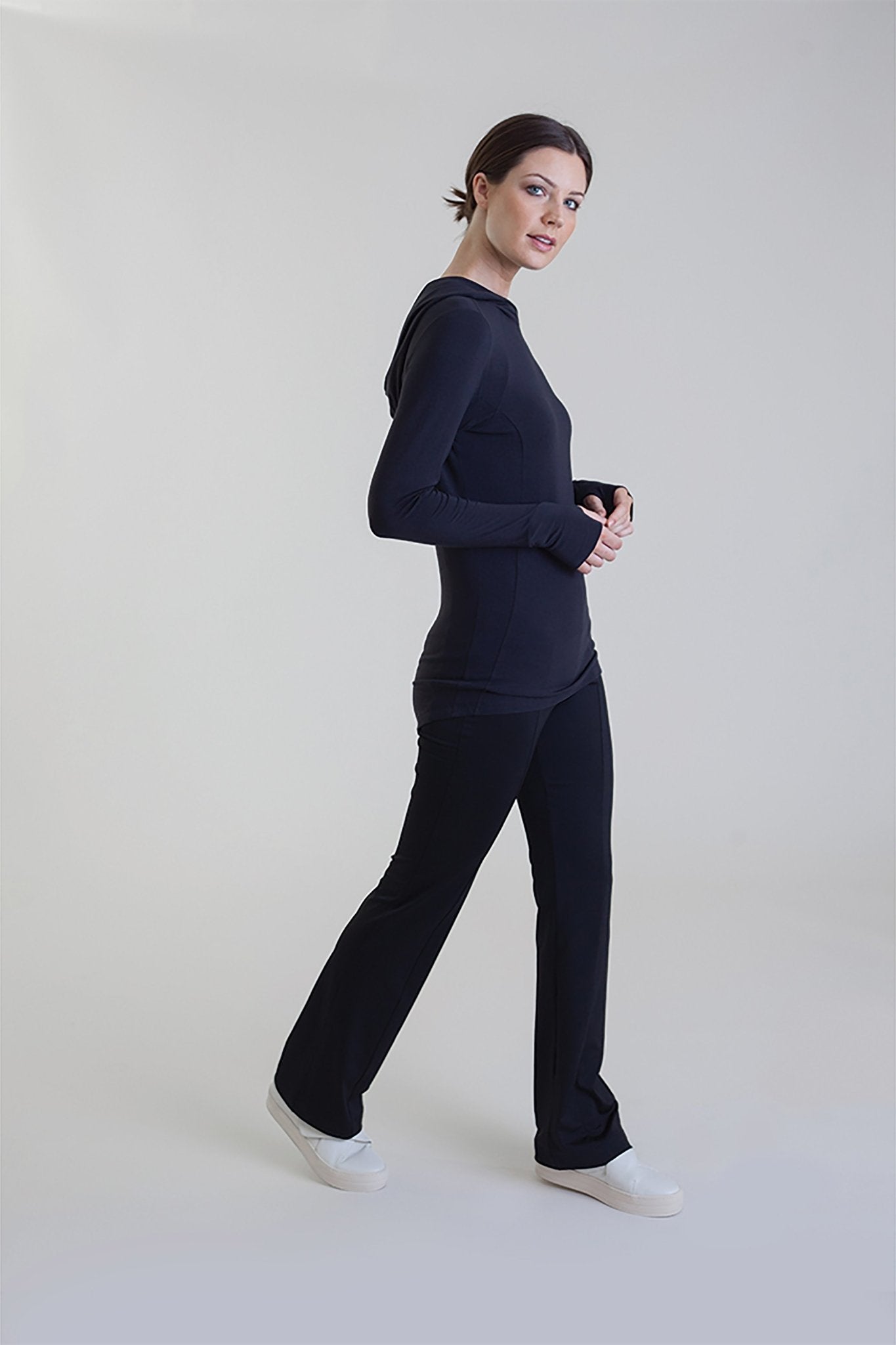 Full body side view of a female model wearing black pants and the Comfort Collagen Hoodie - L'Atelier Global