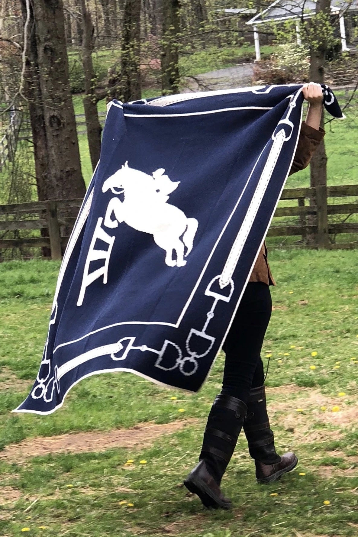 A rider is holding the Equestrian Eco Jumper Throw with both hands, behind her head, fully opened and its blowing in the wind.