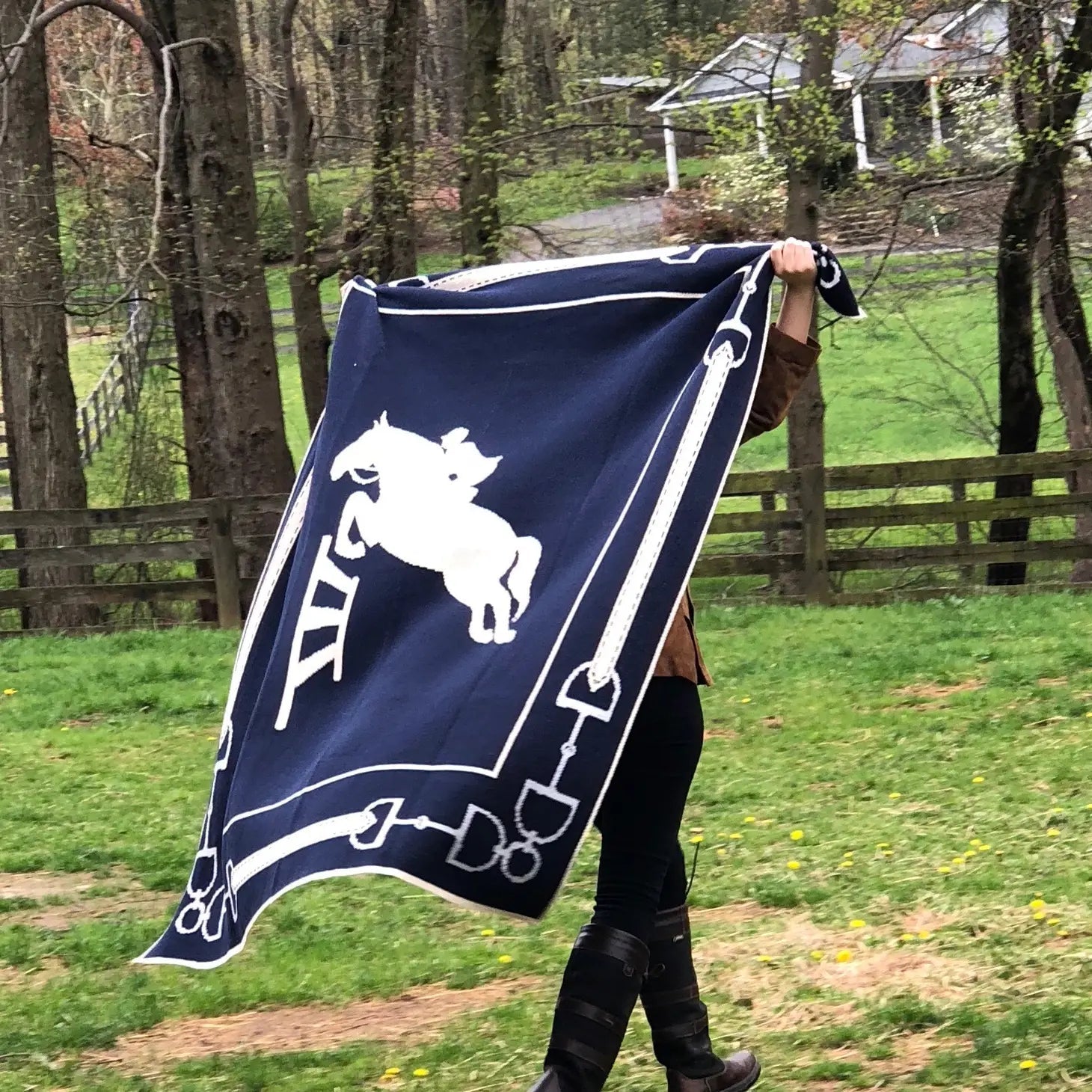 A rider is holding the Equestrian Eco Jumper Throw with both hands, behind her head, fully opened and its blowing in the wind.
